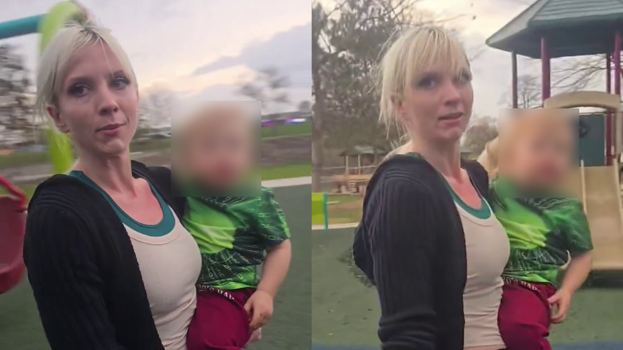A woman with blonde hair holding a child at a playground. The child's face is blurred.