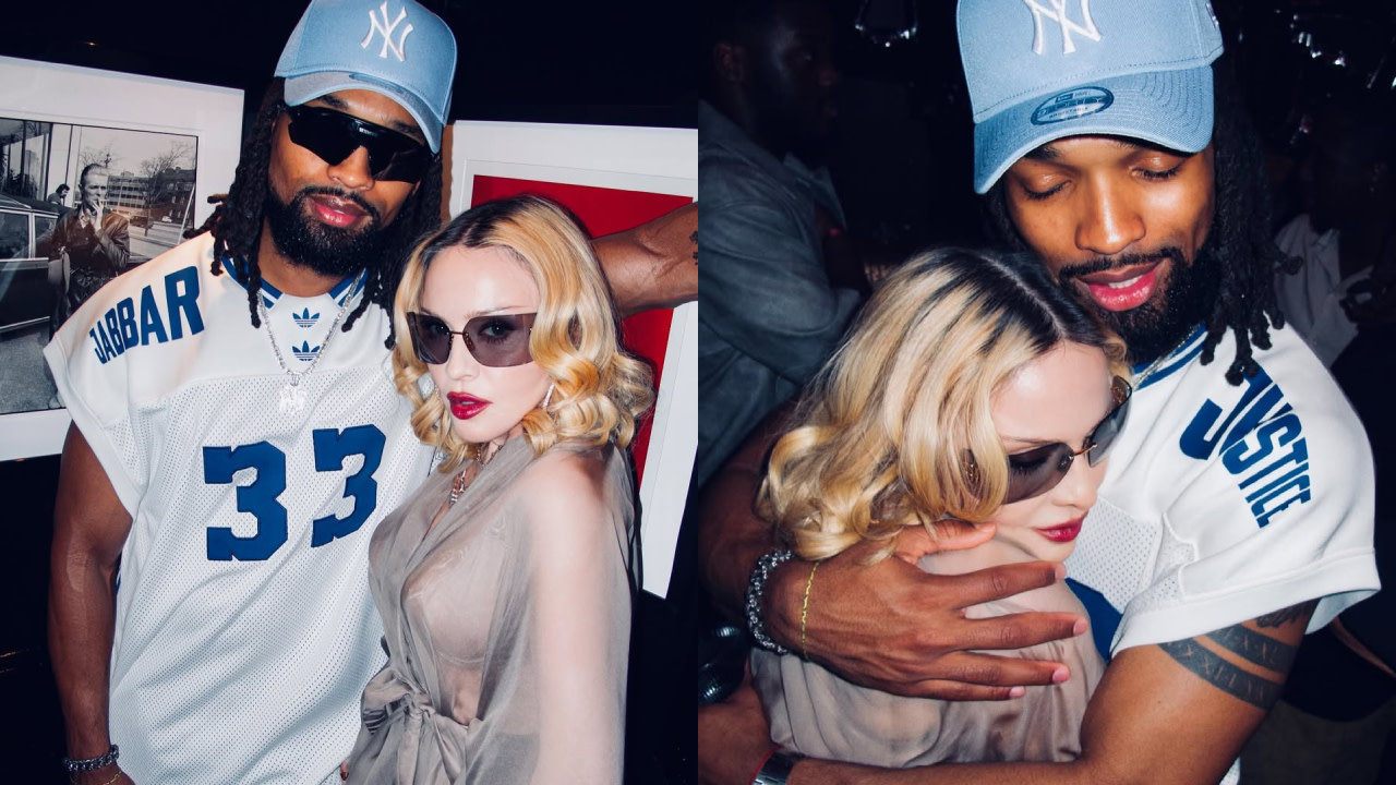 Madonna, wearing sunglasses, is with a man in a sports jersey and cap. They are posing closely in a dimly lit setting.