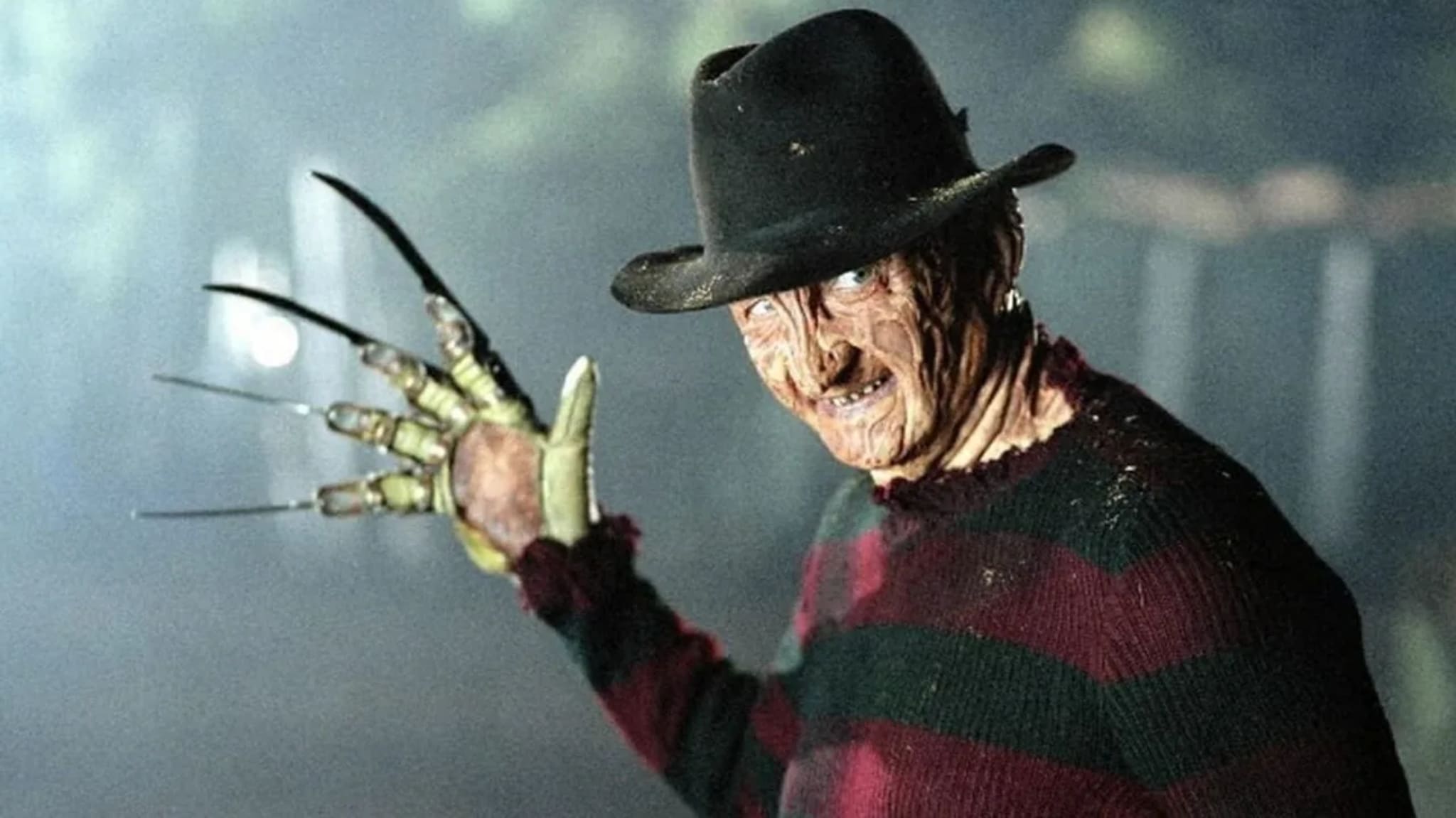Freddy Krueger, wearing a fedora and striped sweater, with a glove of blades, in a foggy setting.