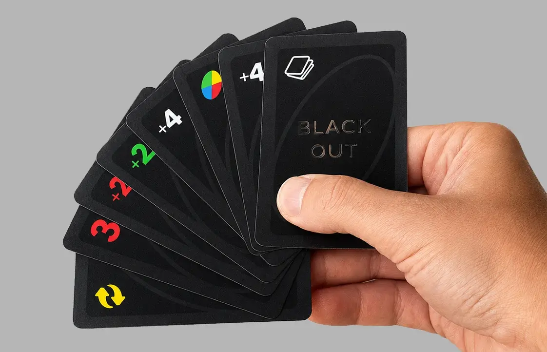 A hand holding a fan of black playing cards with various symbols and numbers, including "+4" and "BLACK OUT."