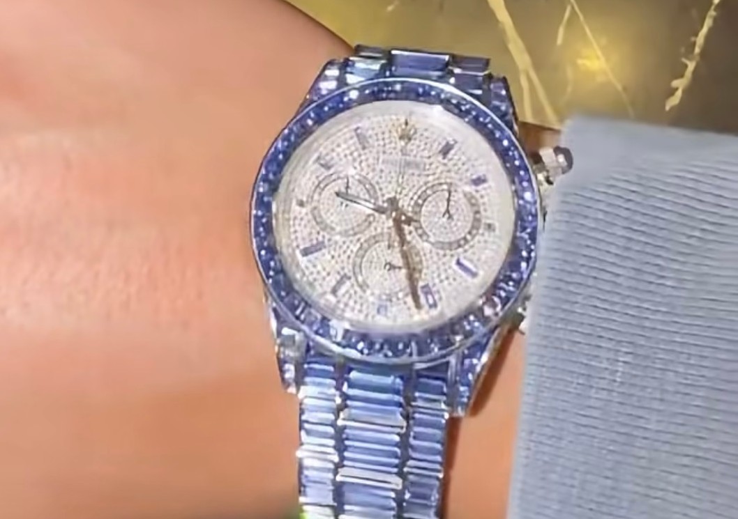A close-up of a wrist wearing a luxurious, diamond-encrusted watch with a silver and blue band.