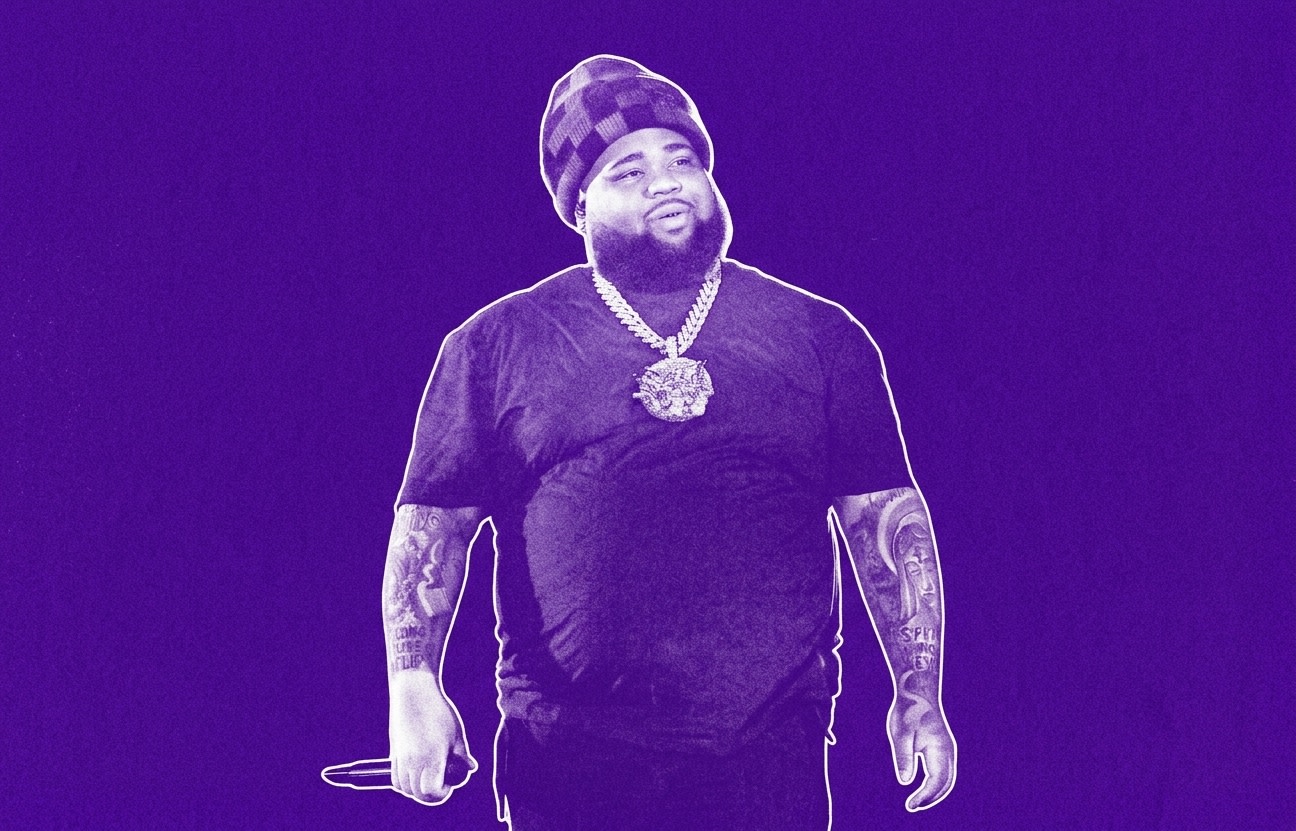 Rod Wave wearing a checkered beanie, black shirt, and large chain necklace, holding a microphone, against a purple background. He has one of the best rap albums of 2026.