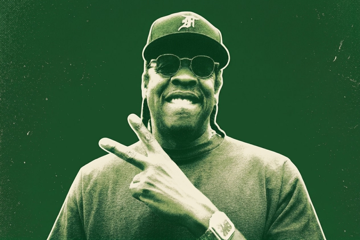A man wearing sunglasses and a cap makes a peace sign at a stadium event. The crowd is visible in the background.