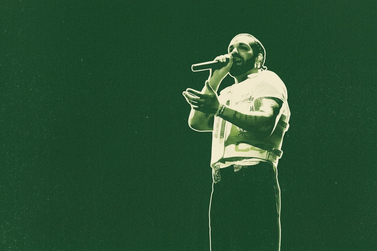 A person performing on stage with a microphone, wearing a white shirt and dark pants, set against a green background.