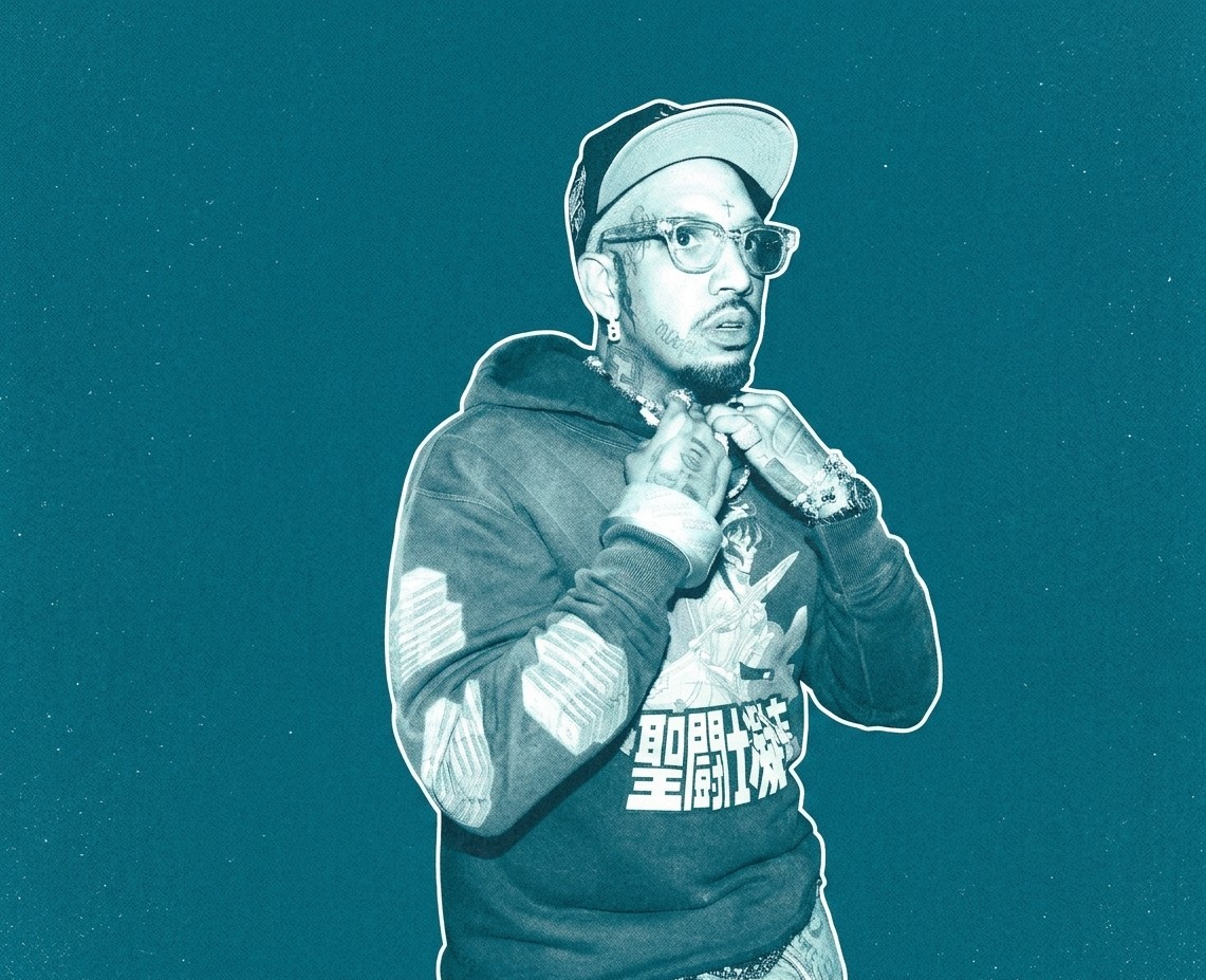 Fenix Flexing wearing a hoodie and cap, adjusting their collar, with glasses and tattoos, set against a teal background.