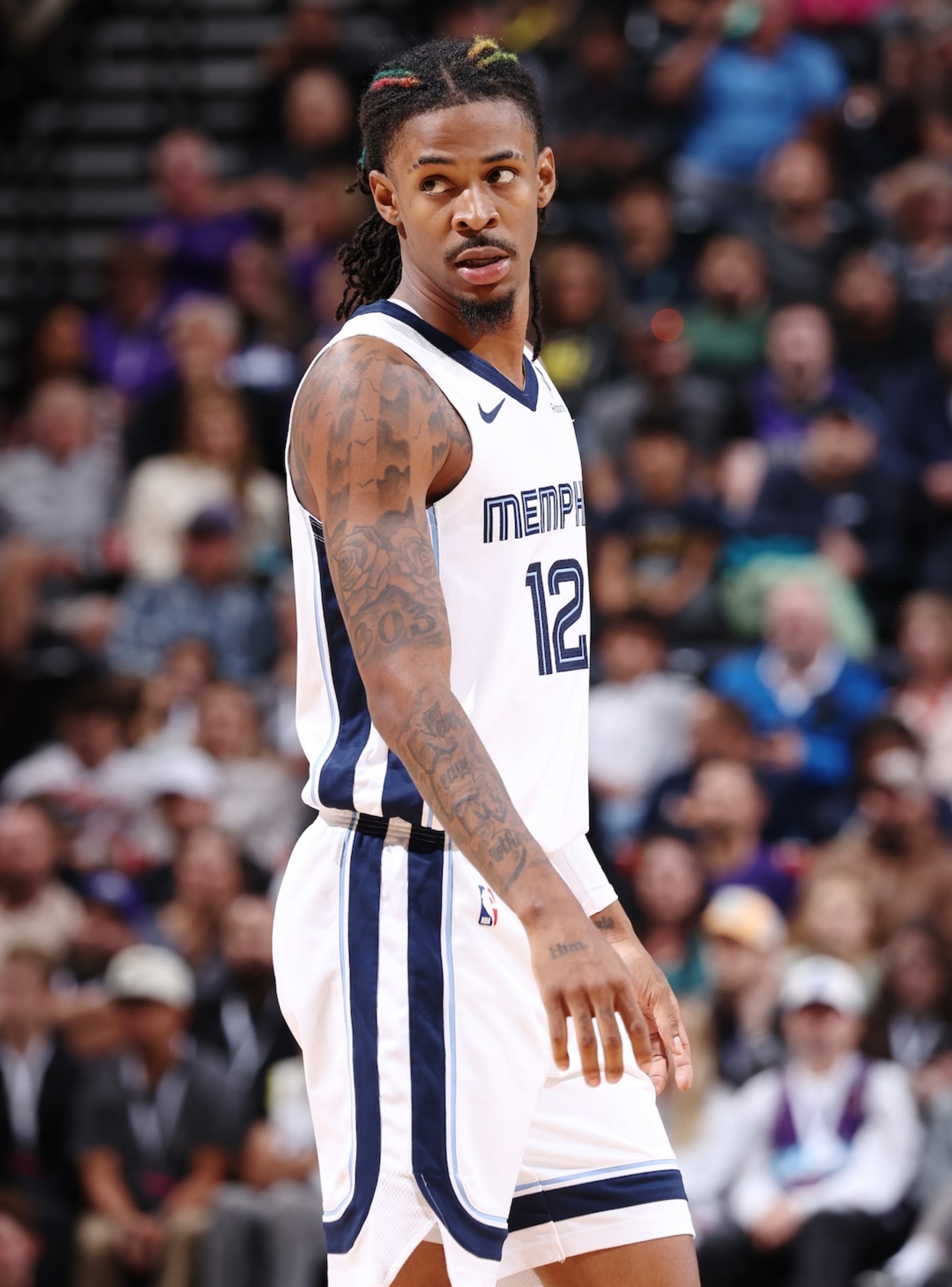 Ja Morant in a Memphis jersey with number 12, standing on the court, looking to the side. Crowd in the background.