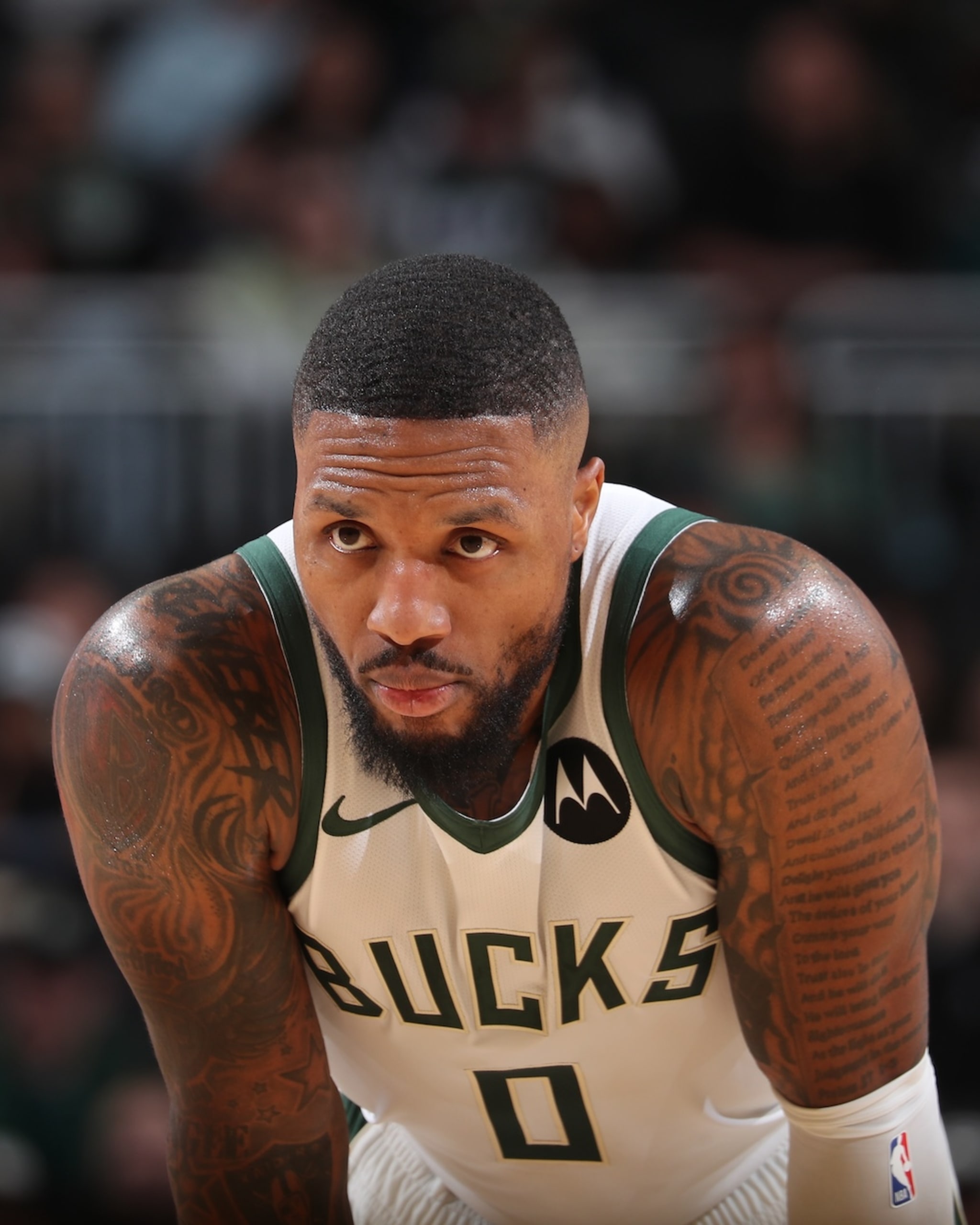 Damian Lillard in a Milwaukee Bucks jersey, number 0, focused during a game, with tattoos on his arms.