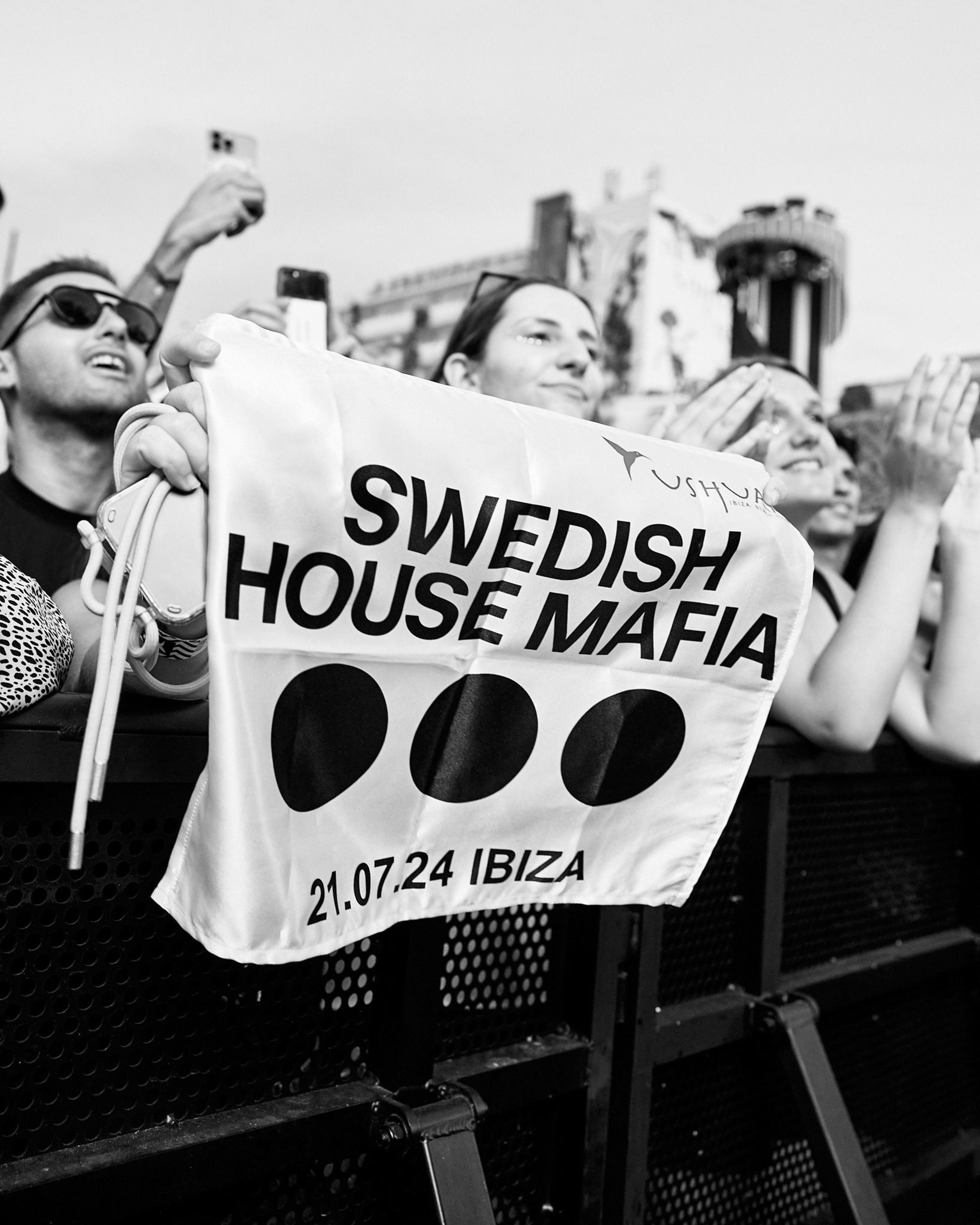 Fans at a Swedish House Mafia concert hold a flag reading "Swedish House Mafia 21.07.24 Ibiza."