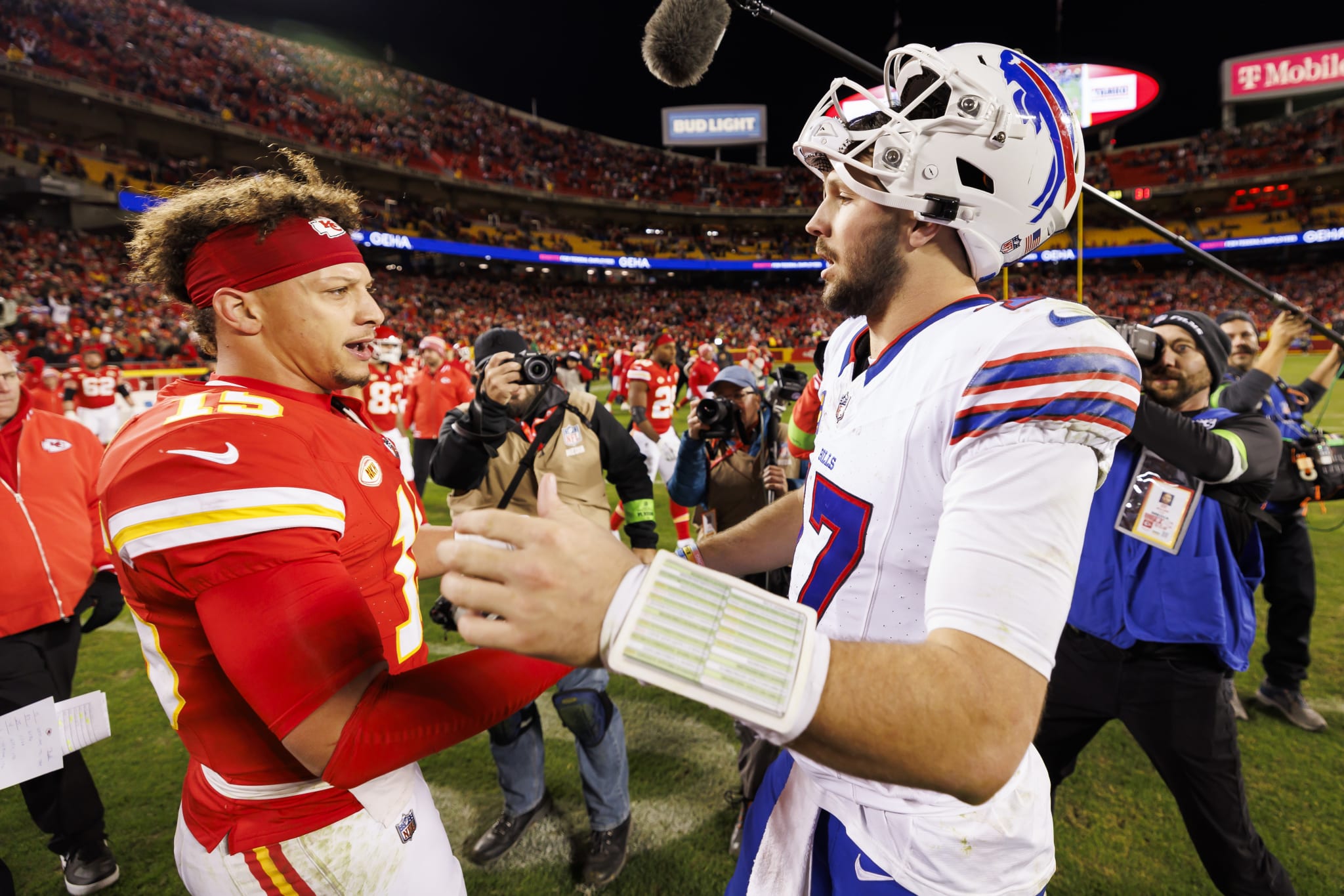 Patrick Mahomes and Josh Allen shake hands on the football field, surrounded by photographers and fans in a stadium.