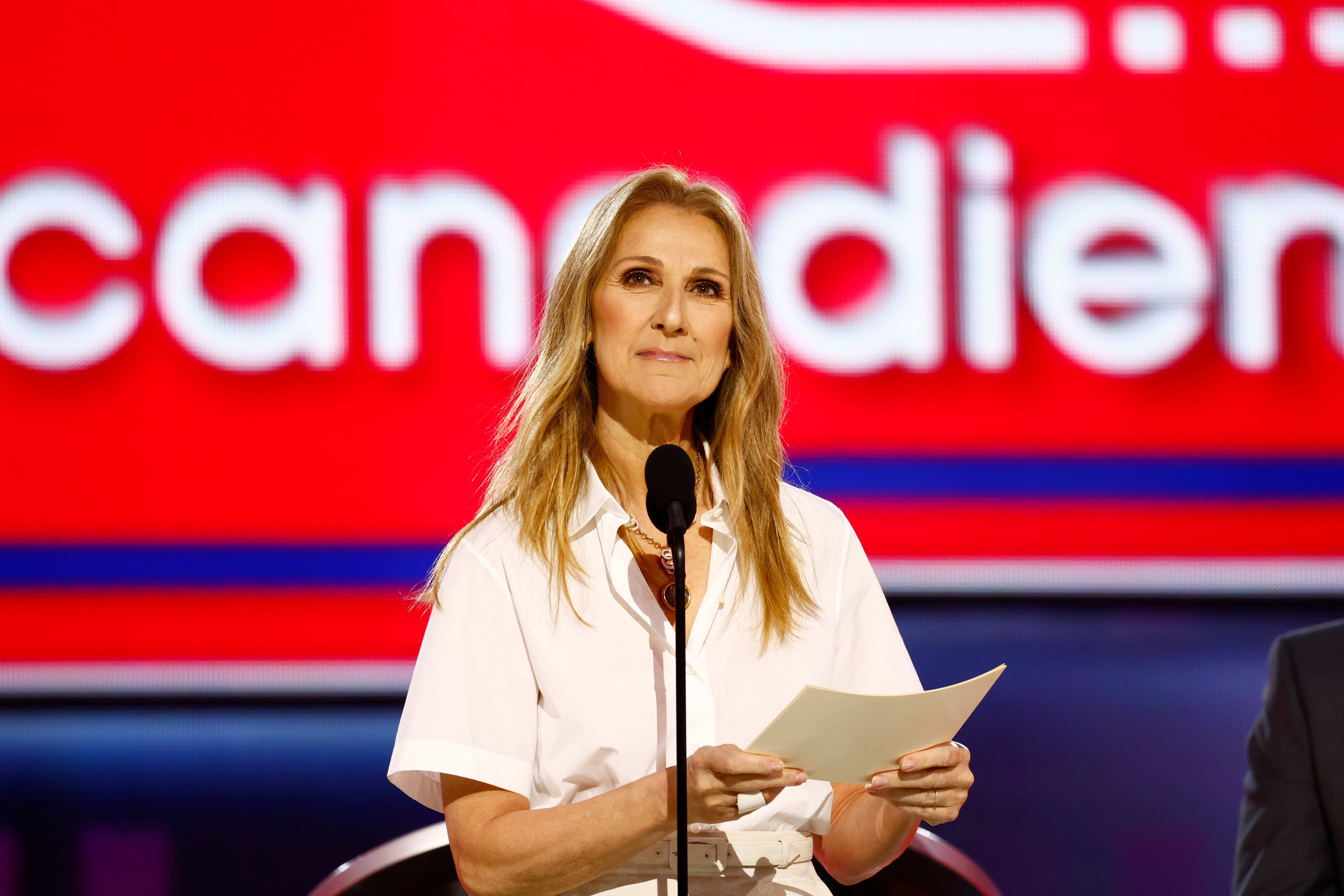 Celine Dion stands behind a microphone with a piece of paper in her hand.