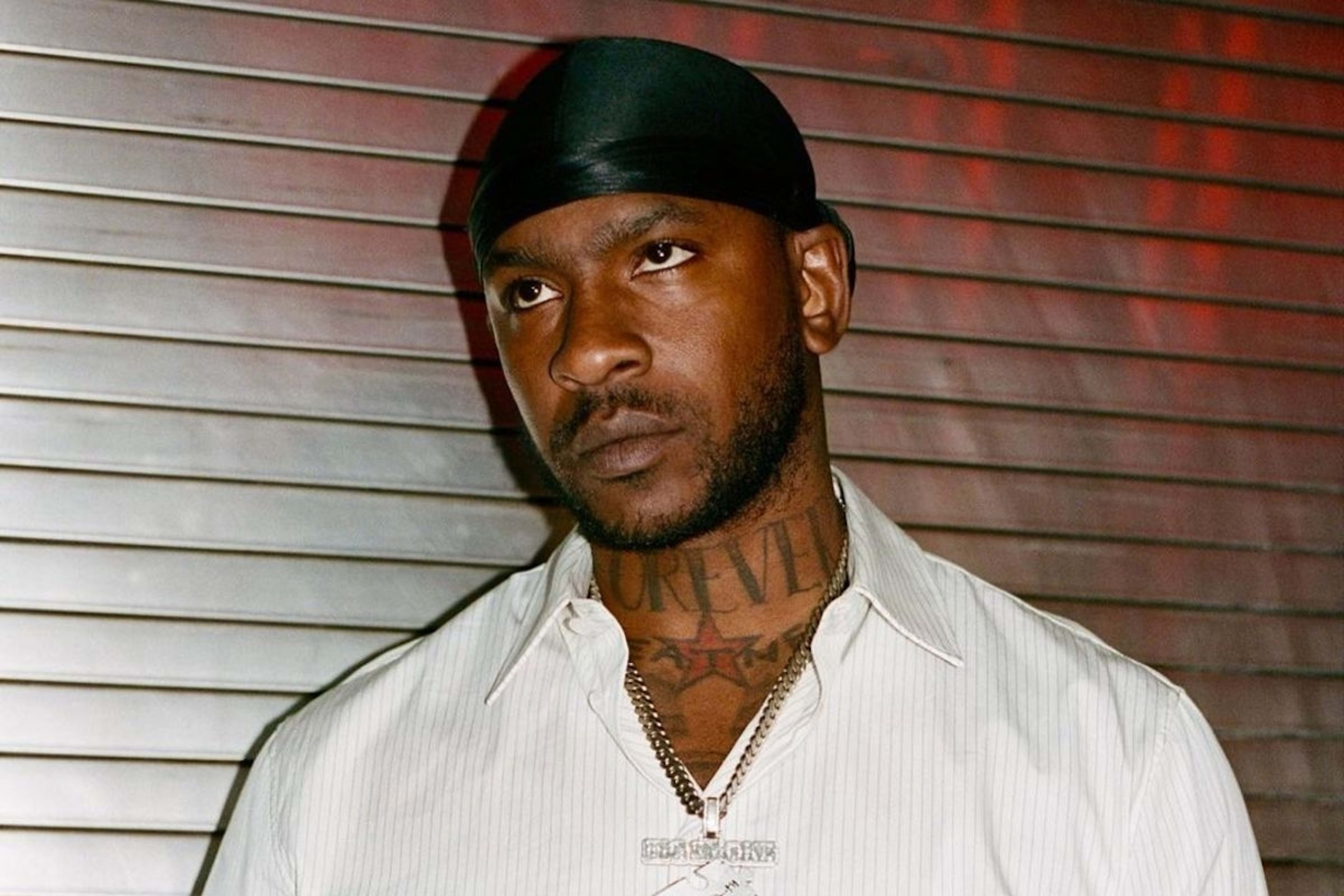 A person wearing a button-up shirt and a chains necklace stands against a metallic background, looking upward