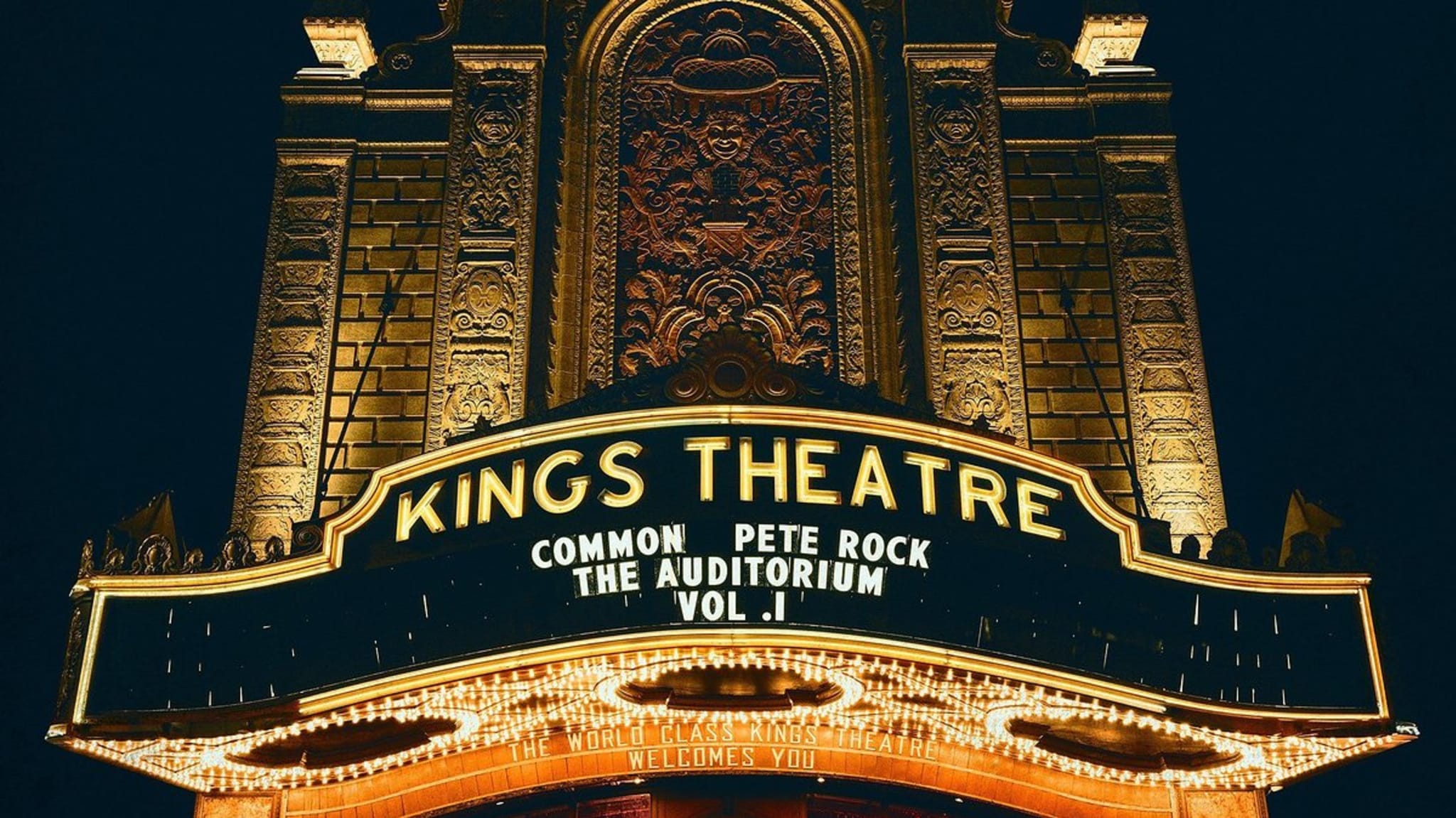 Kings Theatre marquee displays "Common, Pete Rock, The Auditorium Vol. 1." Two people walk in front of the ornate building at night