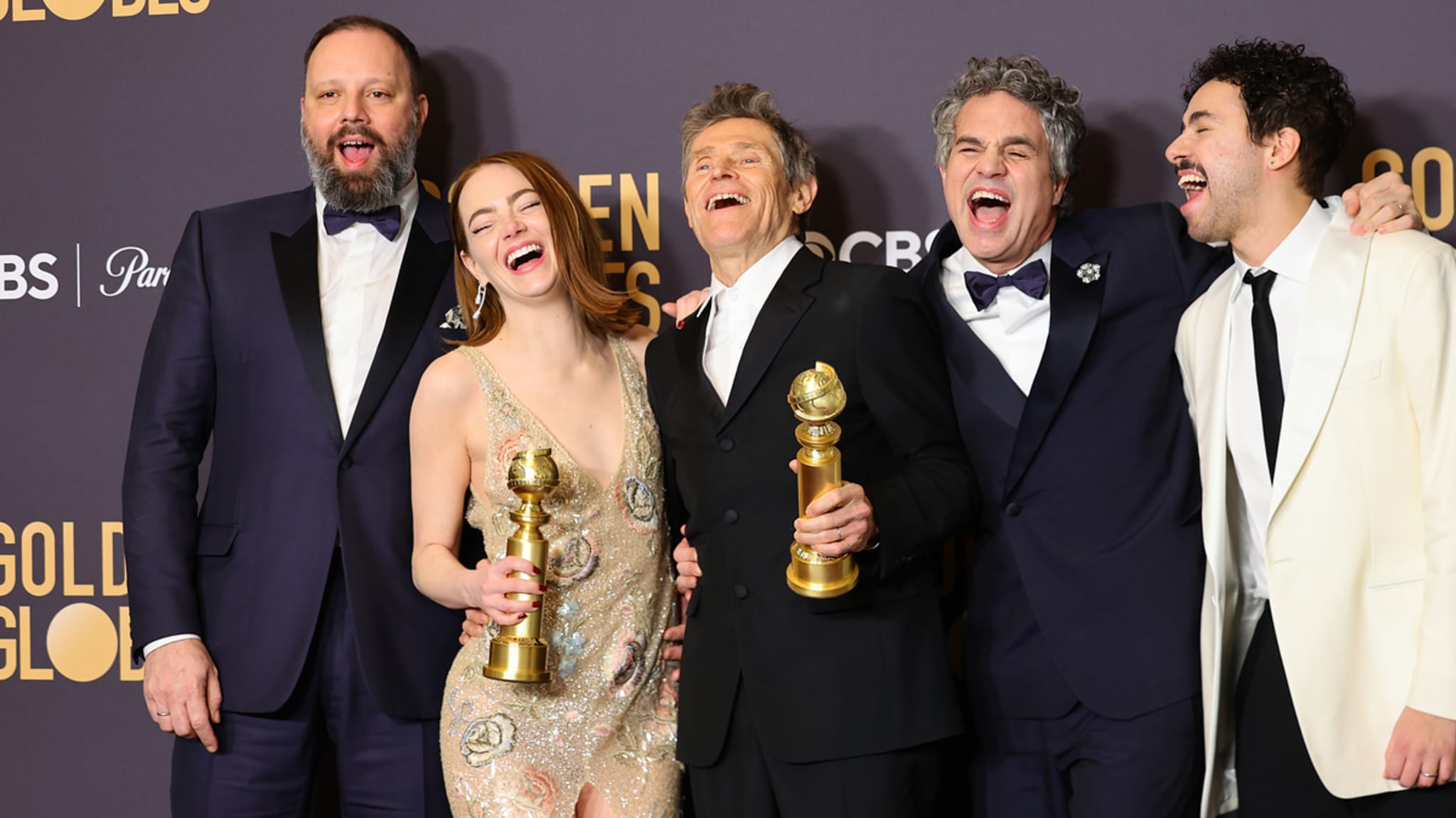 Five actors at the Golden Globes, laughing and holding awards, in formal wear