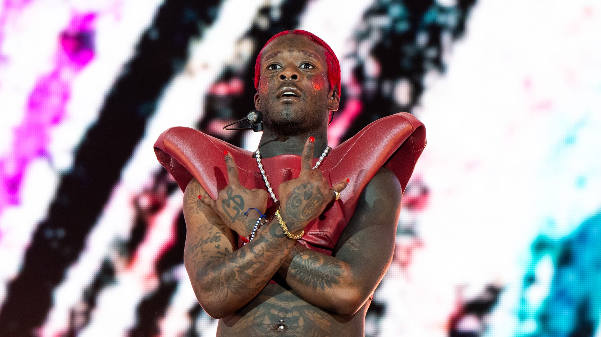 Lil Uzi Vert performing on stage, wearing red attire and shoulder pads, with colorful background visuals.