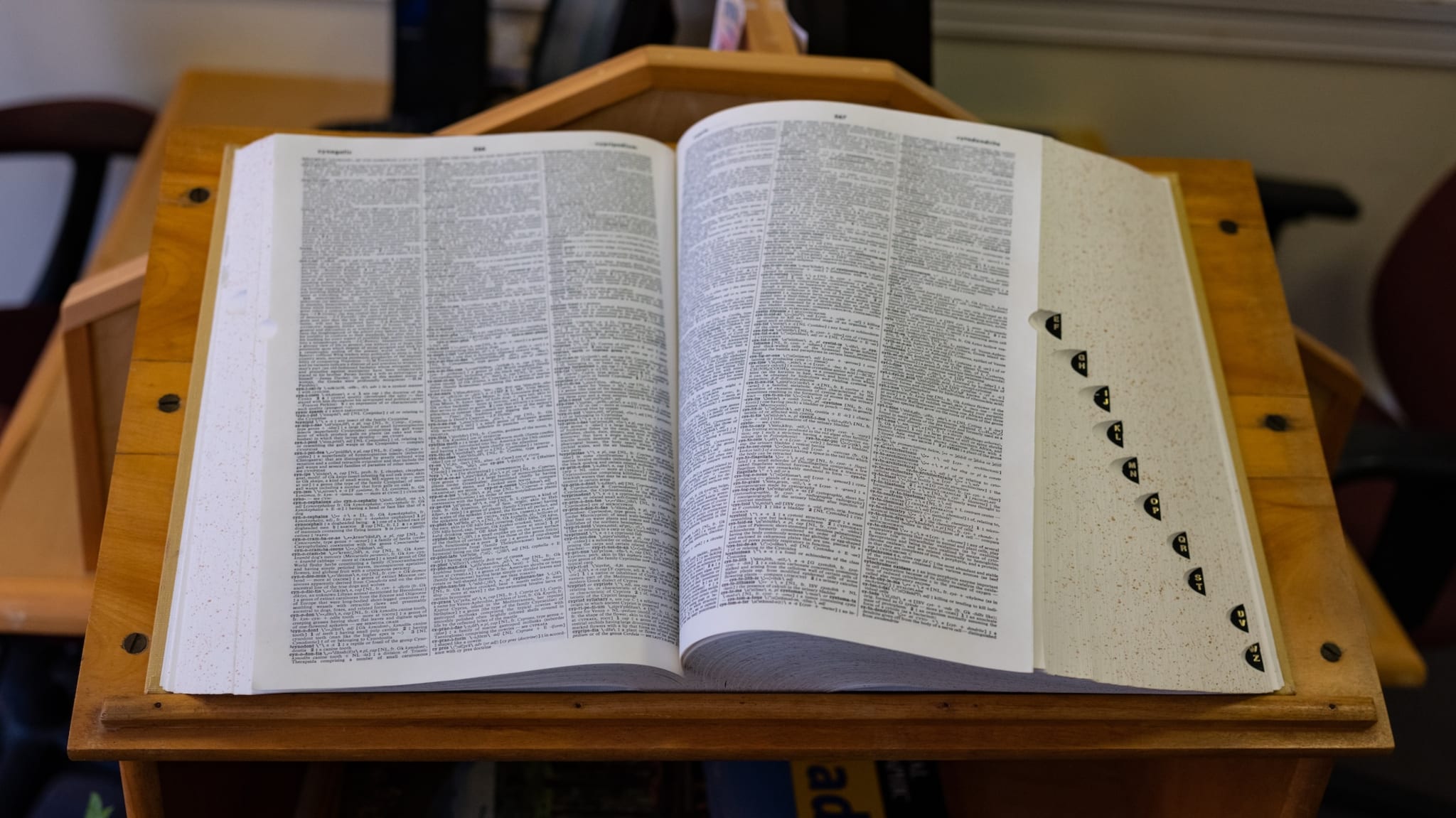 An open dictionary on a wooden stand, displaying densely printed text and index tabs on the right side.