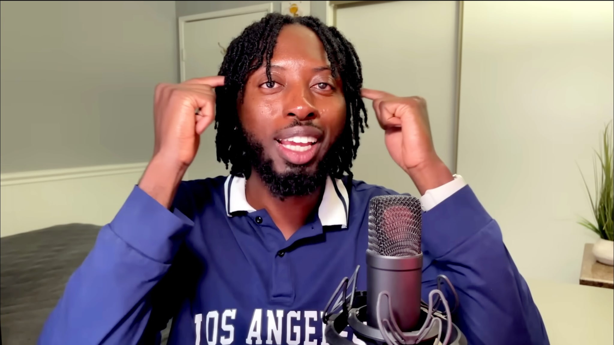 Content Creator XeviUniverse sits in his bedroom with a microphone in front of his face and his fingers on his temples, smirking.