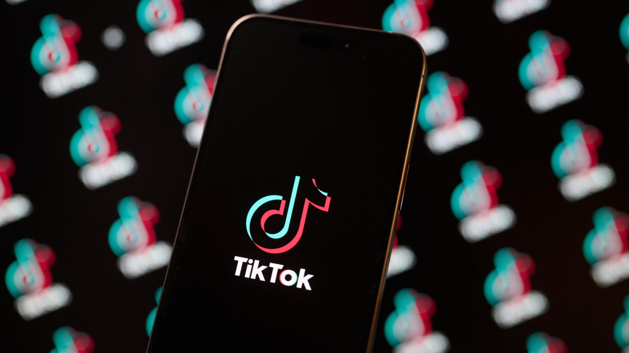 A smartphone displaying the TikTok logo on its screen, with multiple blurred TikTok logos in the background.