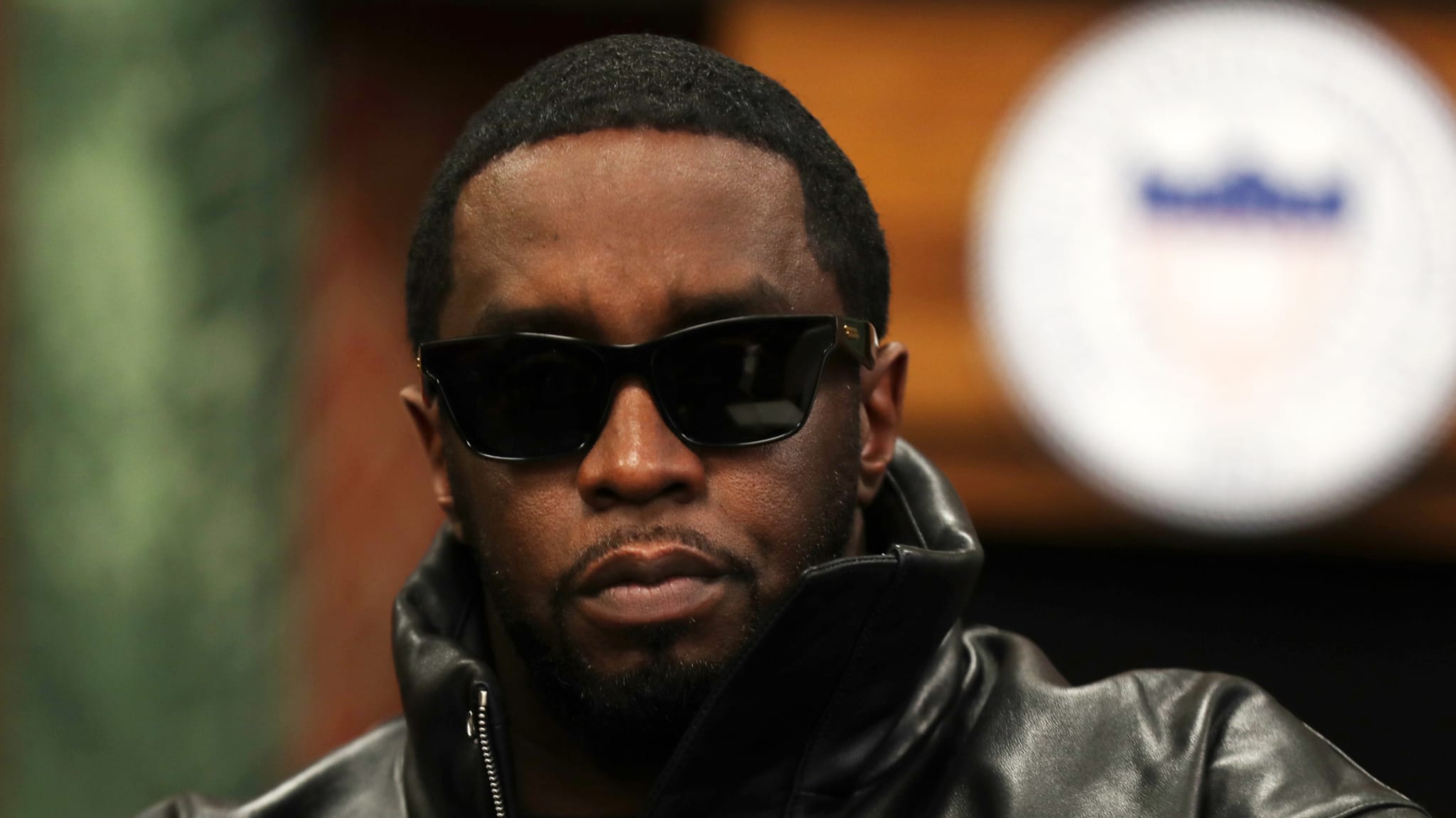 Sean "Diddy" Combs wearing sunglasses and a leather jacket, looking serious.