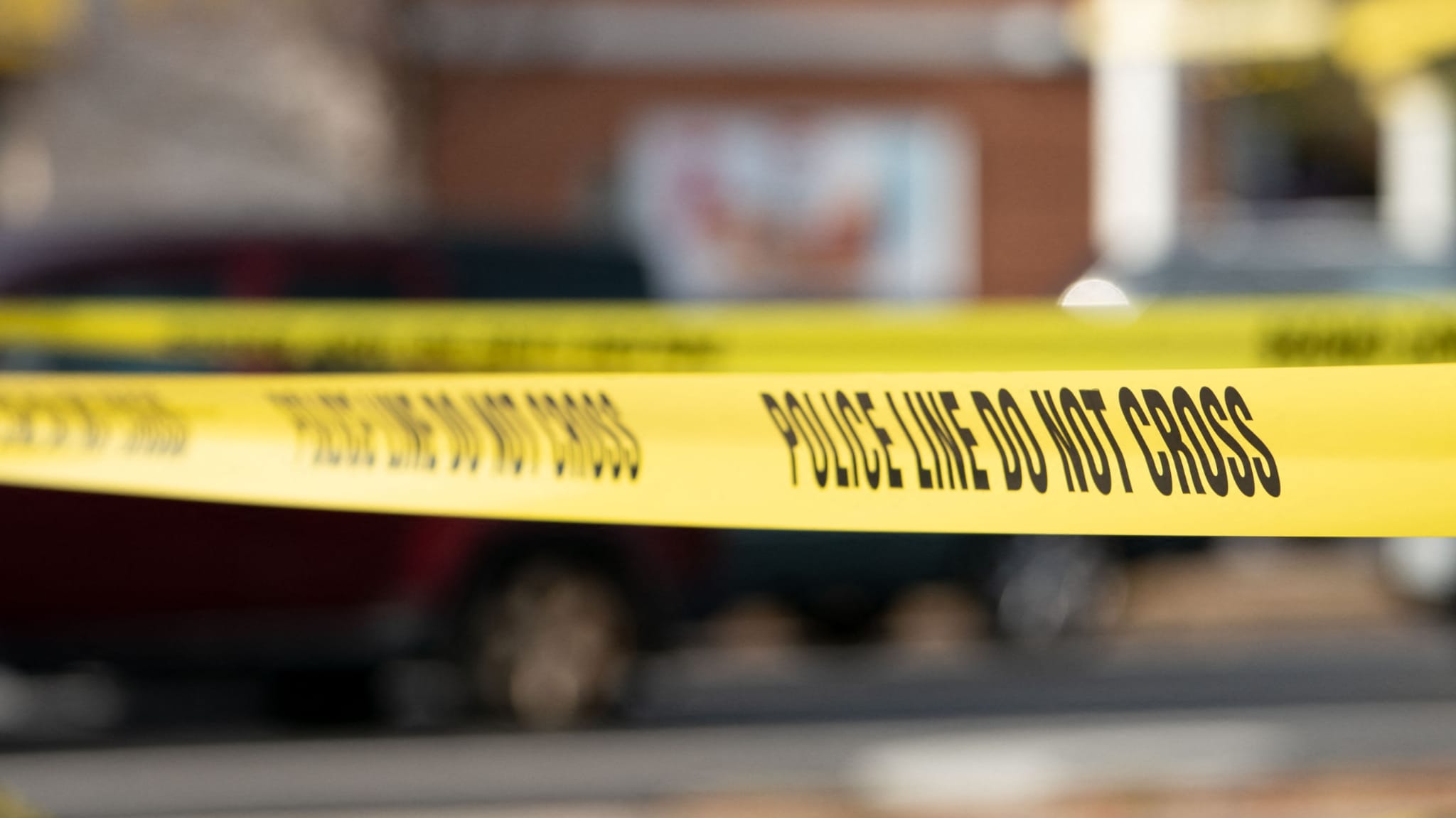 Yellow "Police Line Do Not Cross" tape in focus, with blurred background of a street scene.