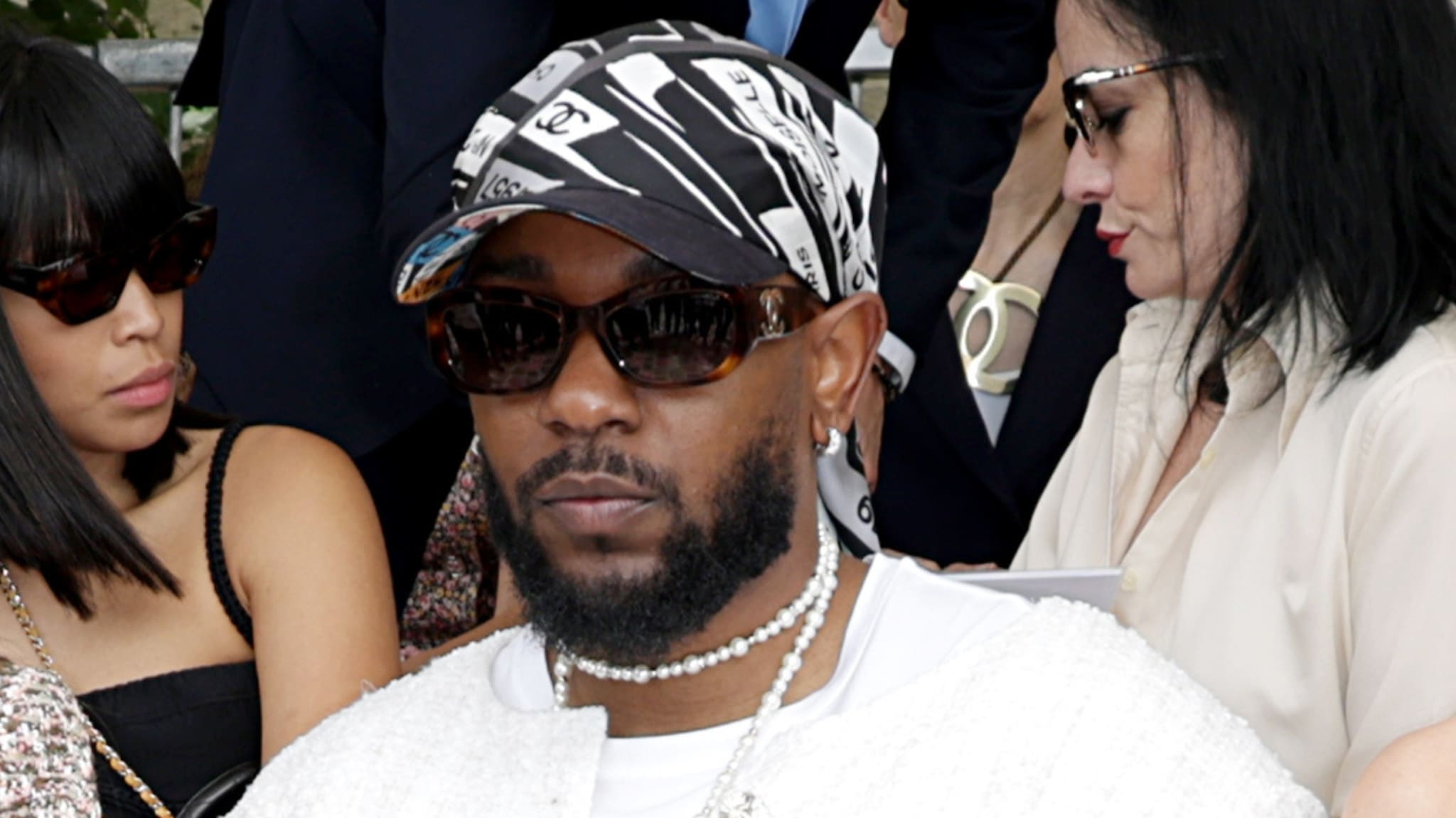 Kendrick Lamar wearing sunglasses and a patterned bandana, seated at an event.