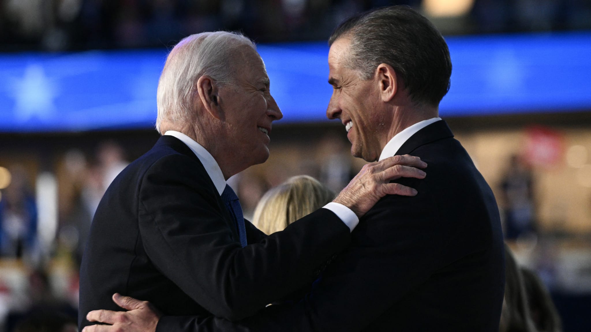 Joe Biden and Hunter Biden embrace, smiling at each other in a warmly lit setting.