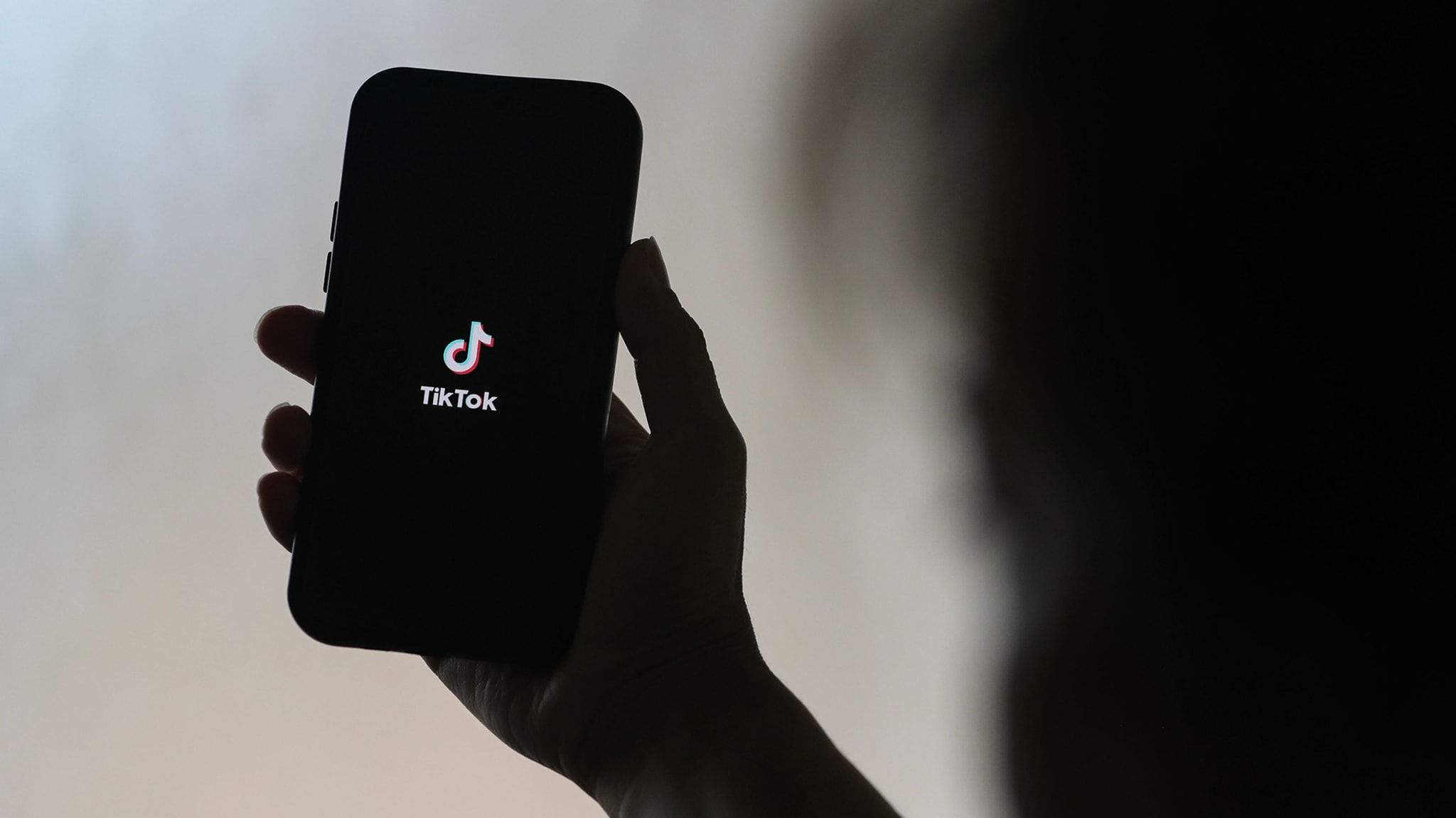 A person holding a smartphone displaying the TikTok logo on the screen.