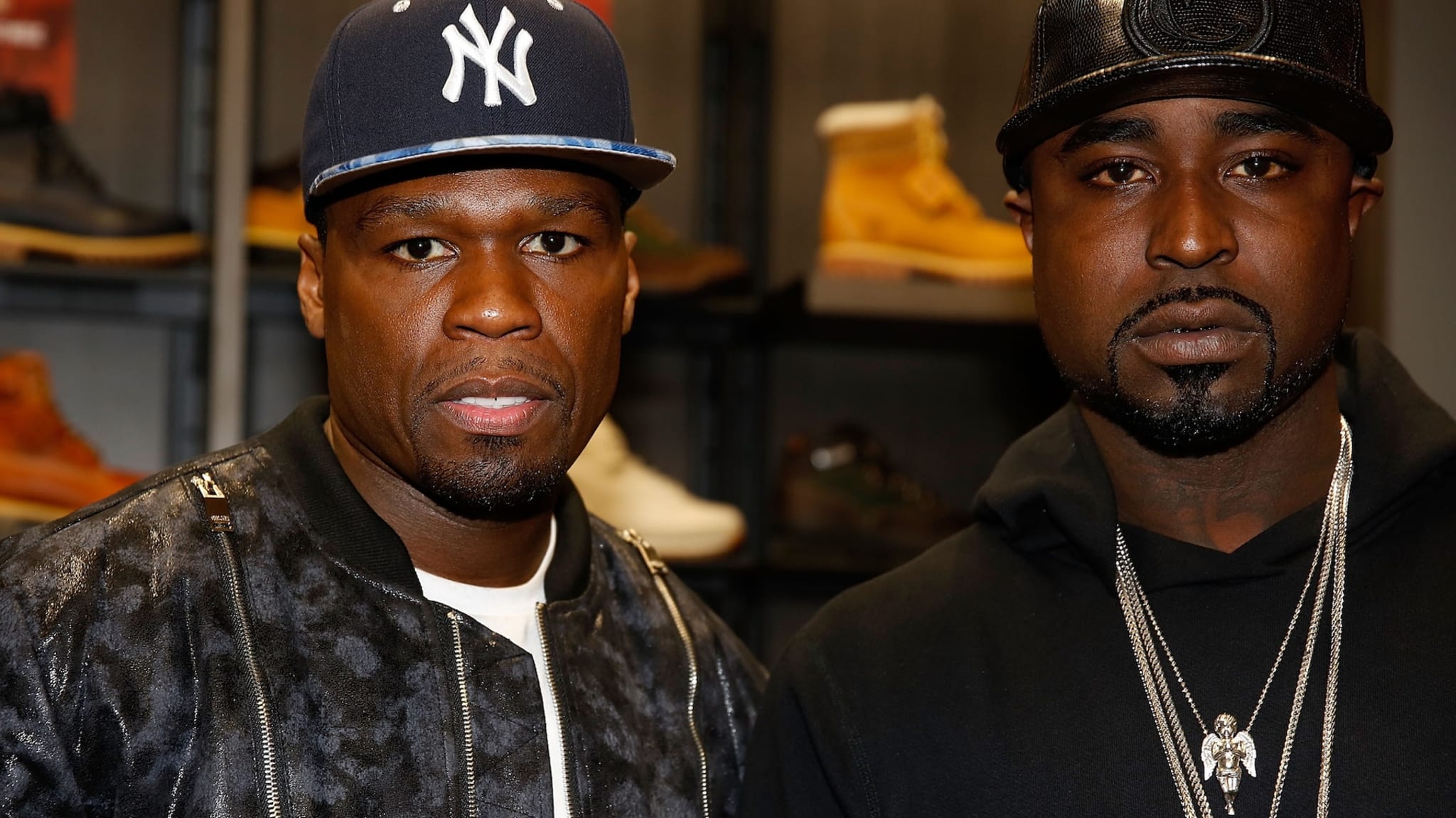 50 Cent and Young Buck, both wearing caps and jackets, posing together in a store with shoes in the background.