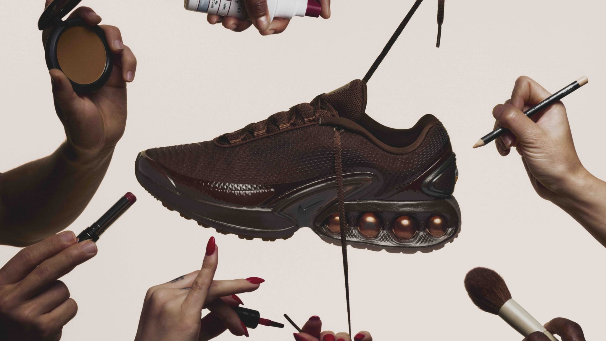 A brown sneaker is surrounded by hands holding makeup items like brushes, lipstick, and powder, against a plain background.