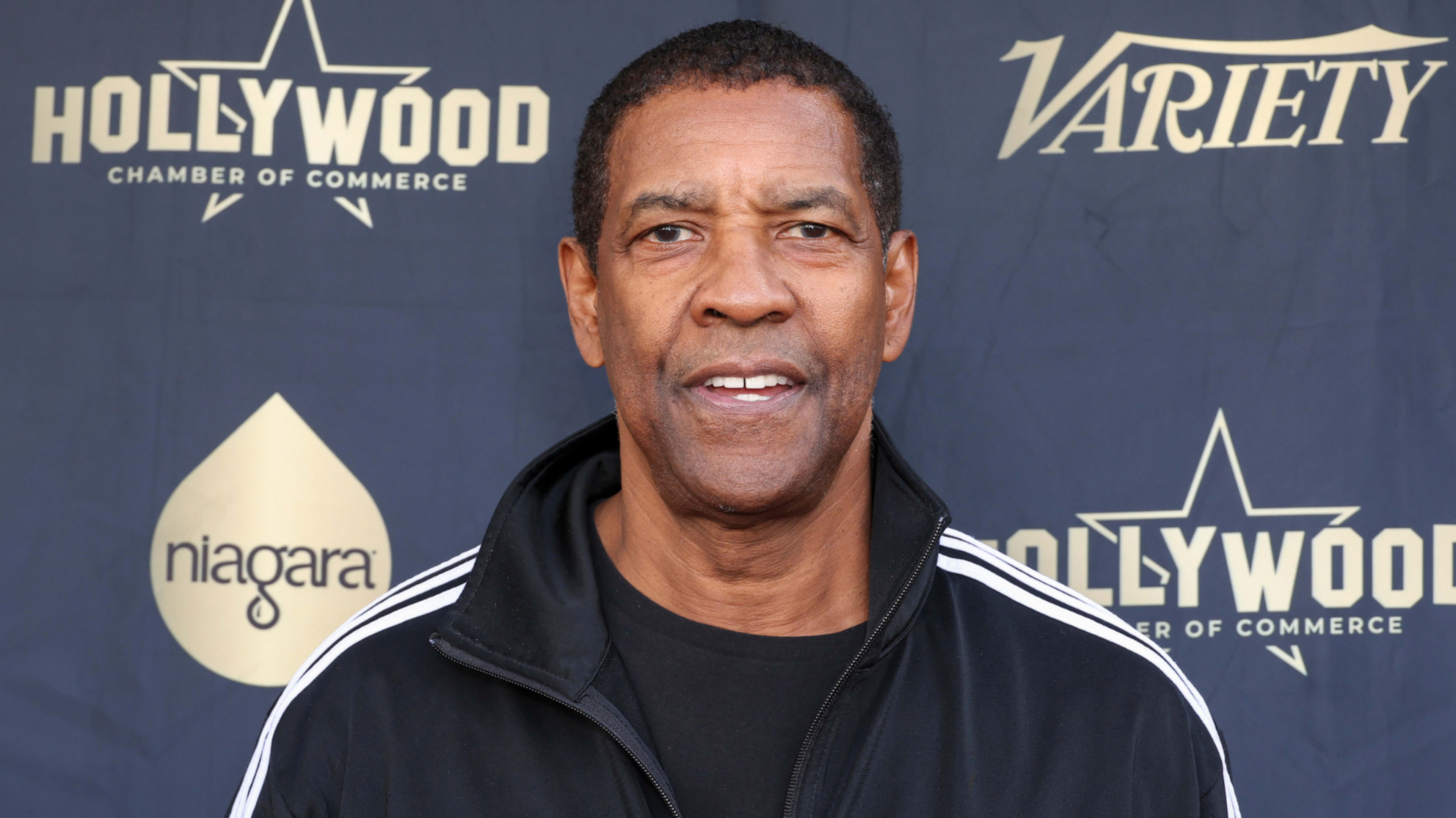 Denzel Washington at a Hollywood Chamber of Commerce event, wearing a black jacket with white stripes on the sleeves