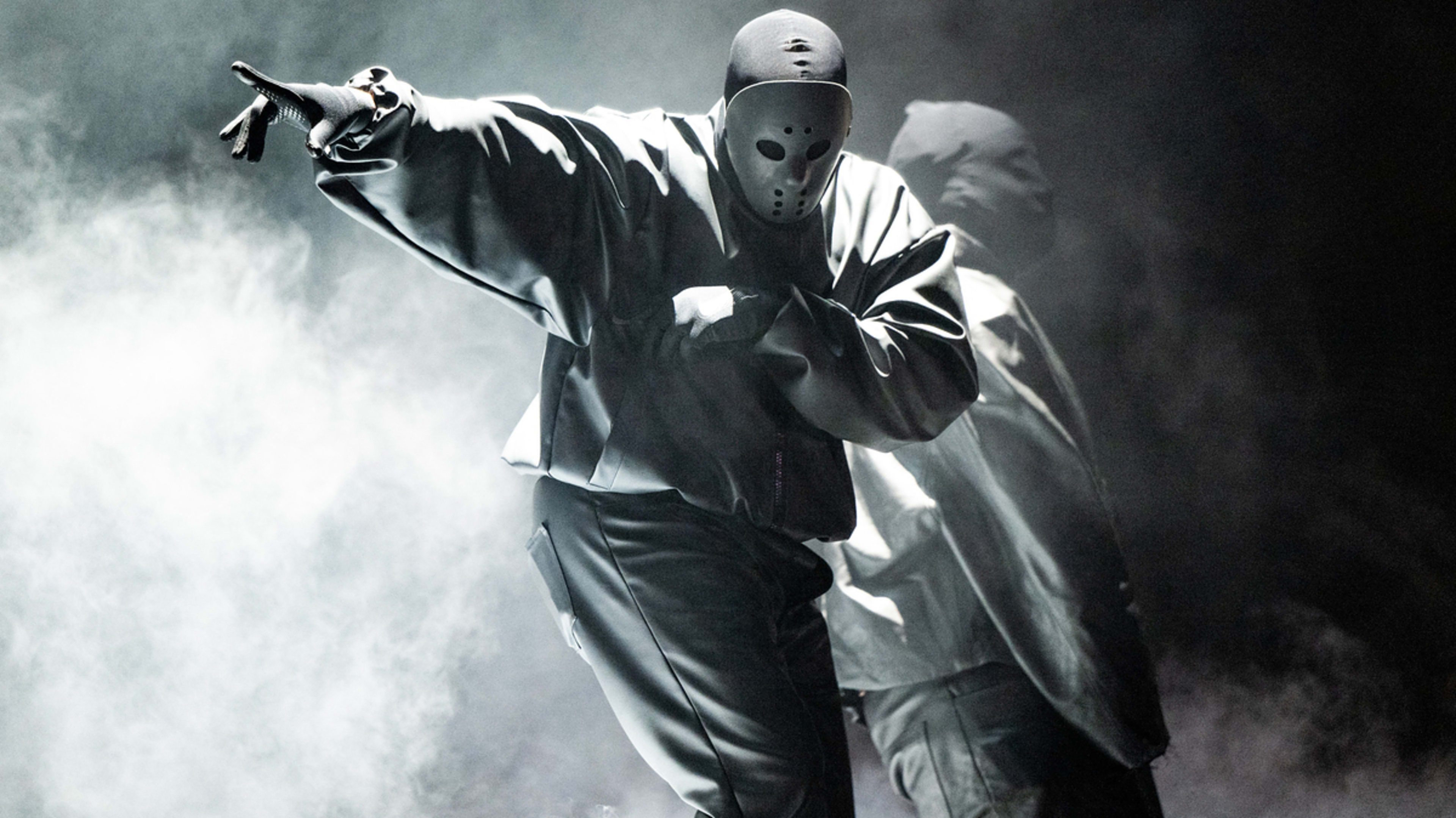 Two masked performers in oversized clothing, striking dynamic poses on a foggy stage during a music performance