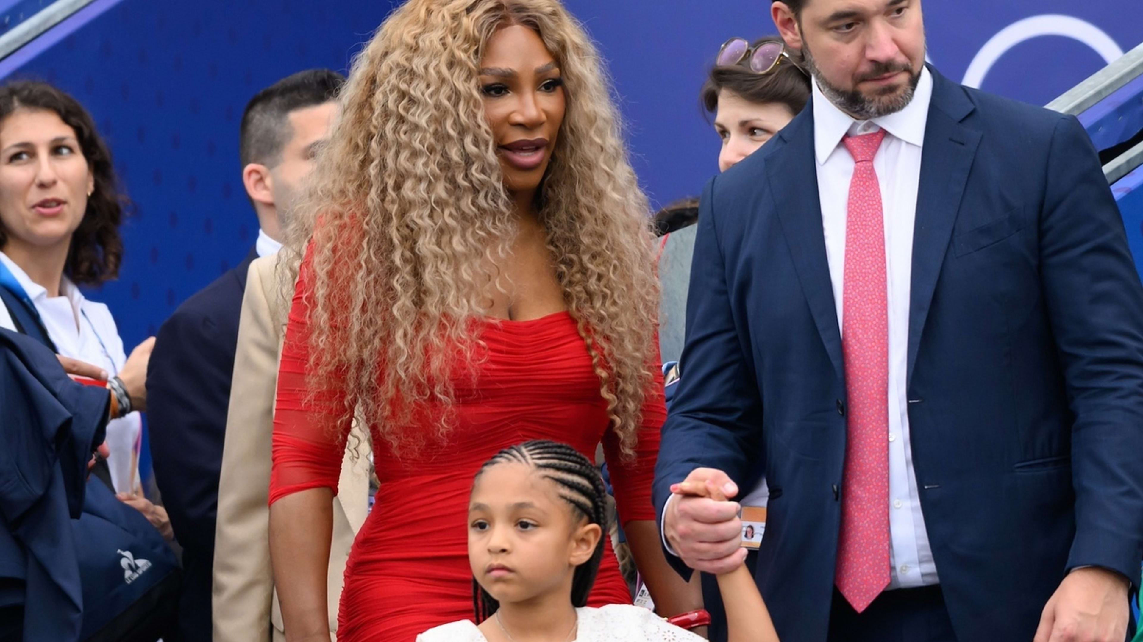 Serena Williams in a form-fitting dress with Alexis Ohanian and their daughter, Alexis Olympia Ohanian Jr., holding hands while being surrounded by people