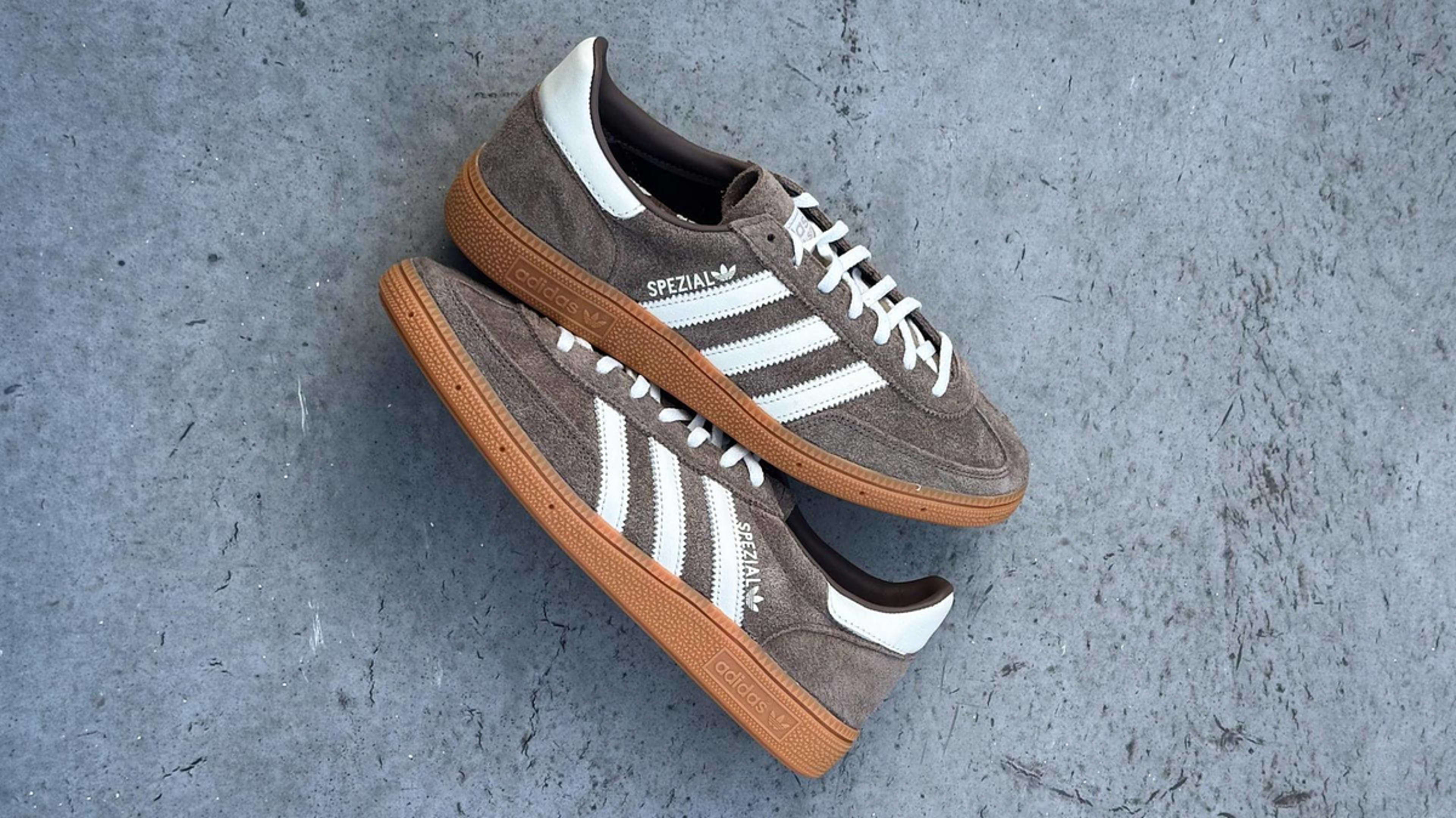 A pair of Adidas Spezial sneakers with white stripes and brown suede material displayed on a gray surface