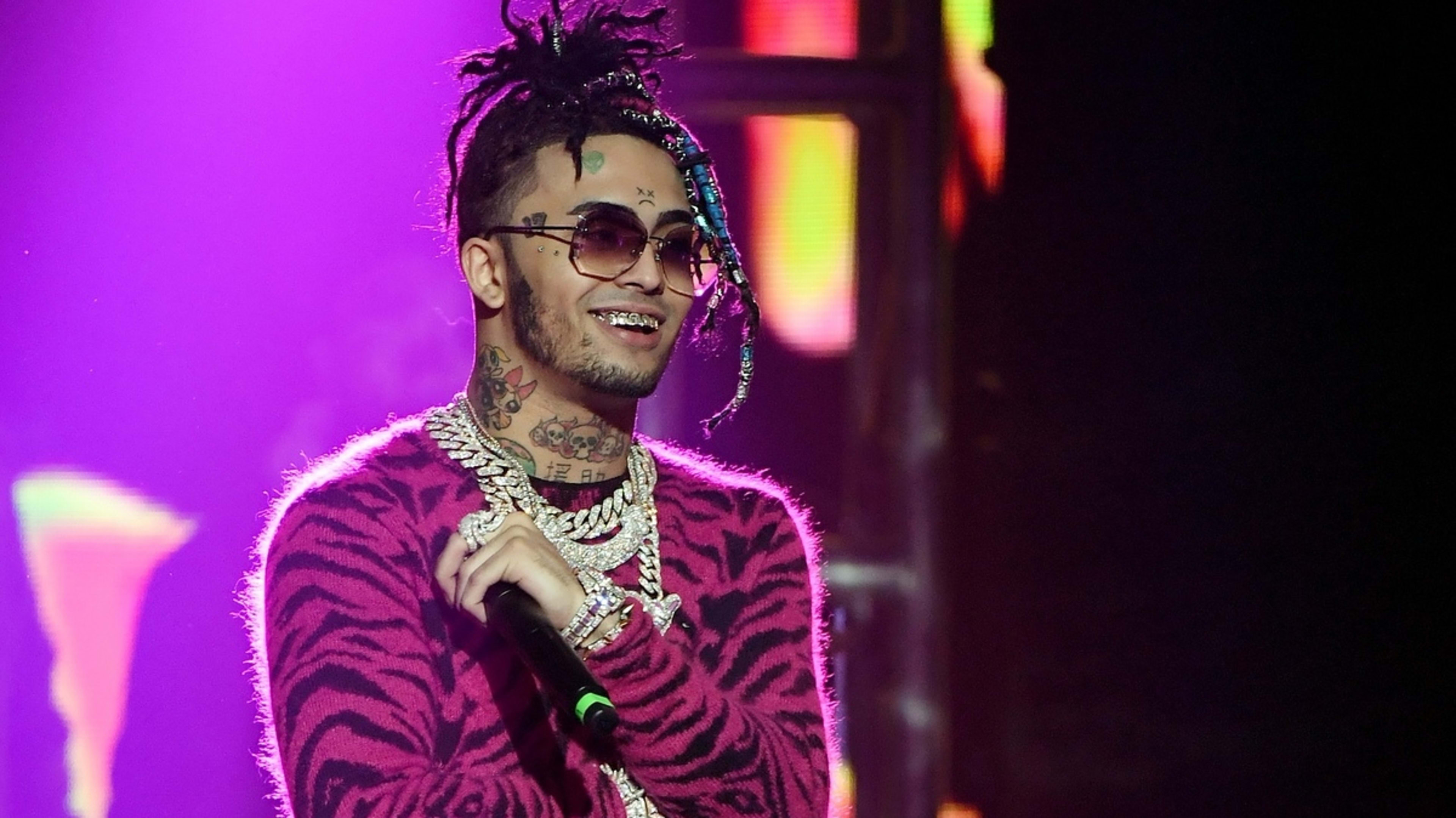 Rap artist Lil Pump performs on stage, wearing sunglasses, a patterned sweater, and multiple chains