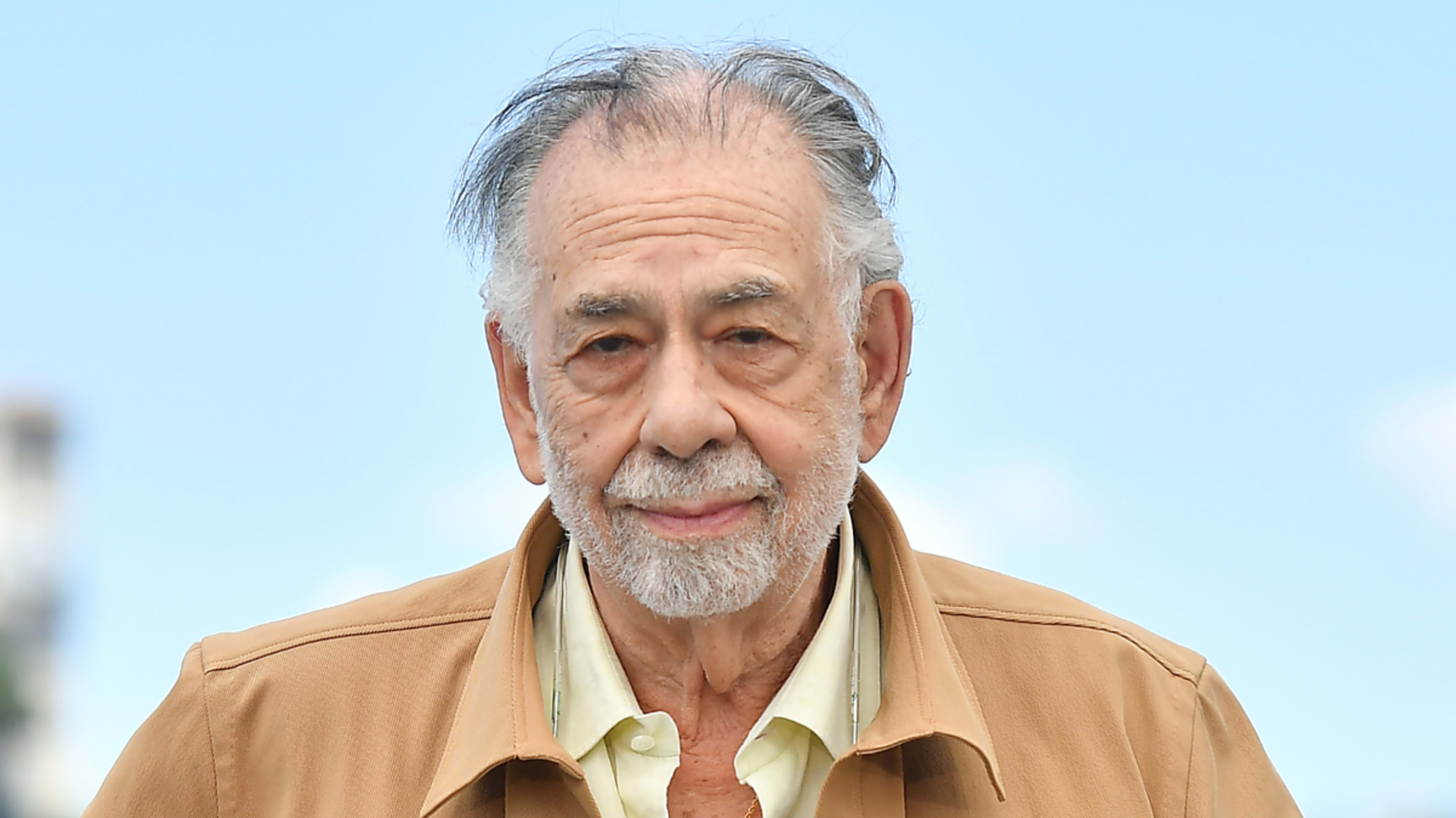 Francis Ford Coppola in a tan jacket and light-colored shirt, standing outdoors