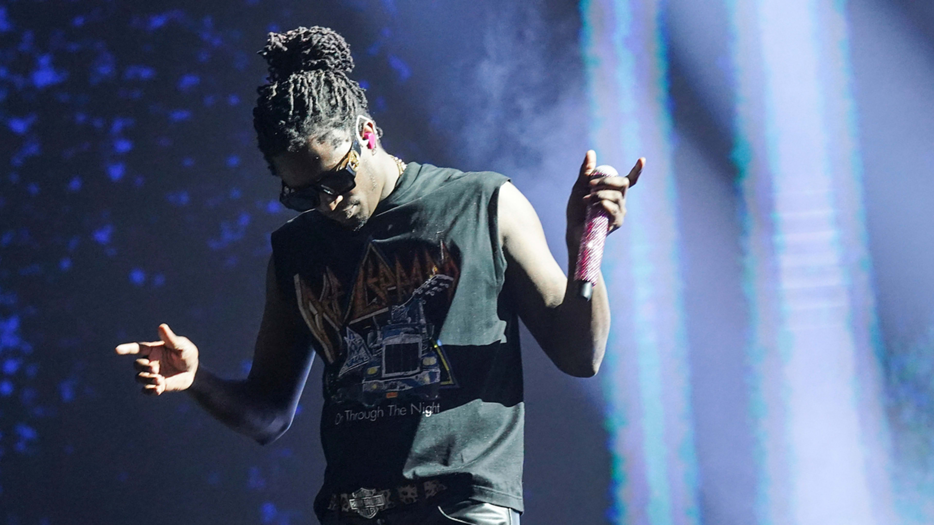 Rapper Young Thug performing on stage, wearing sunglasses and a sleeveless graphic t-shirt