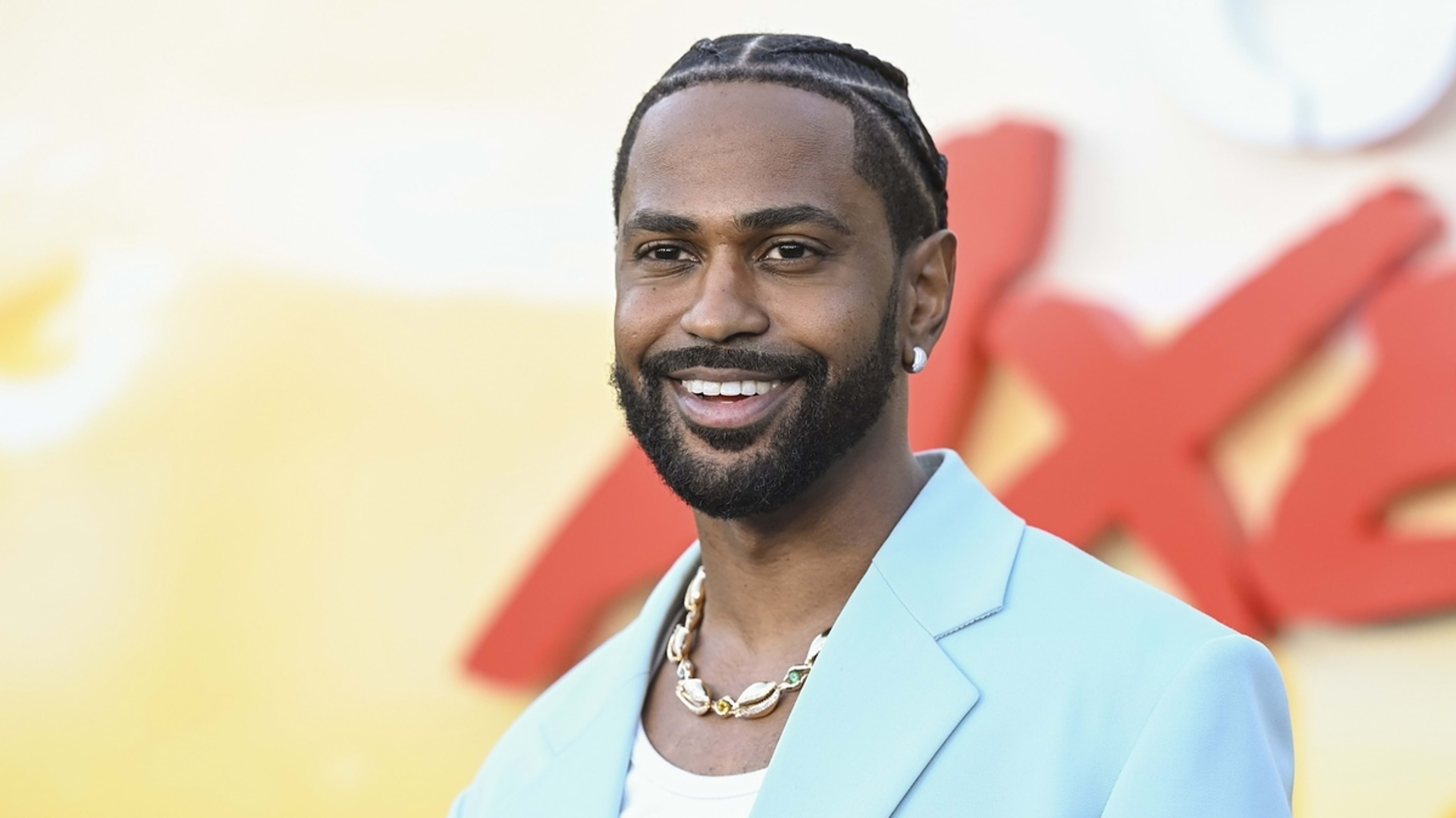 Big Sean smiles while wearing a light blazer and a chunky necklace at a red carpet event