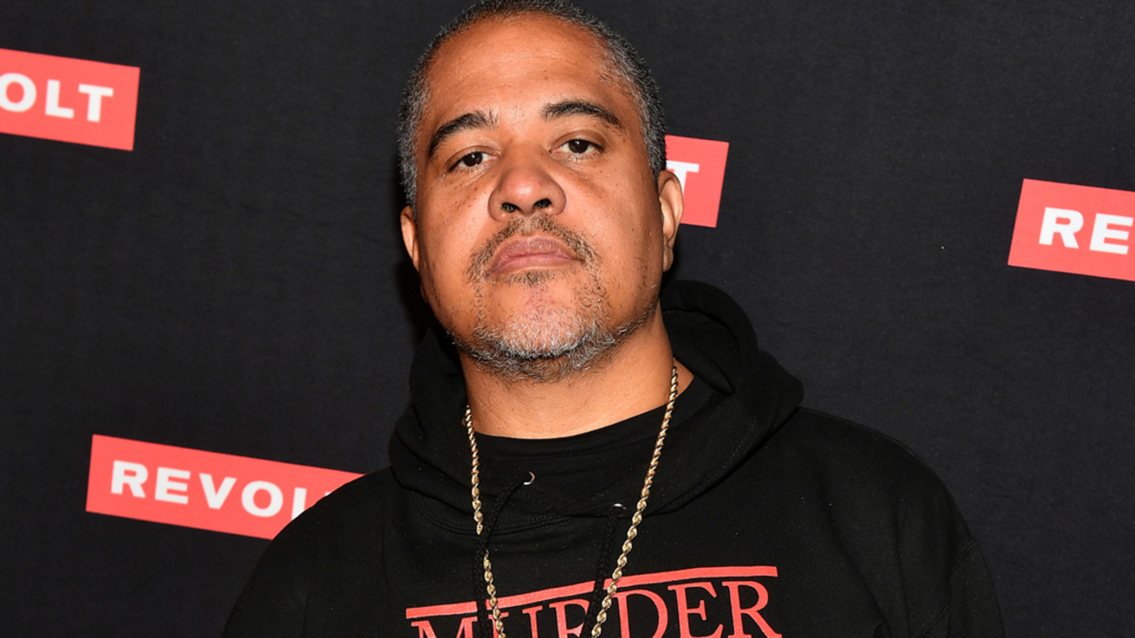 I don't know who this is. Person stands in front of a step and repeat banner, wearing a "Murder Inc Records" hoodie and a chain necklace, making a hand gesture