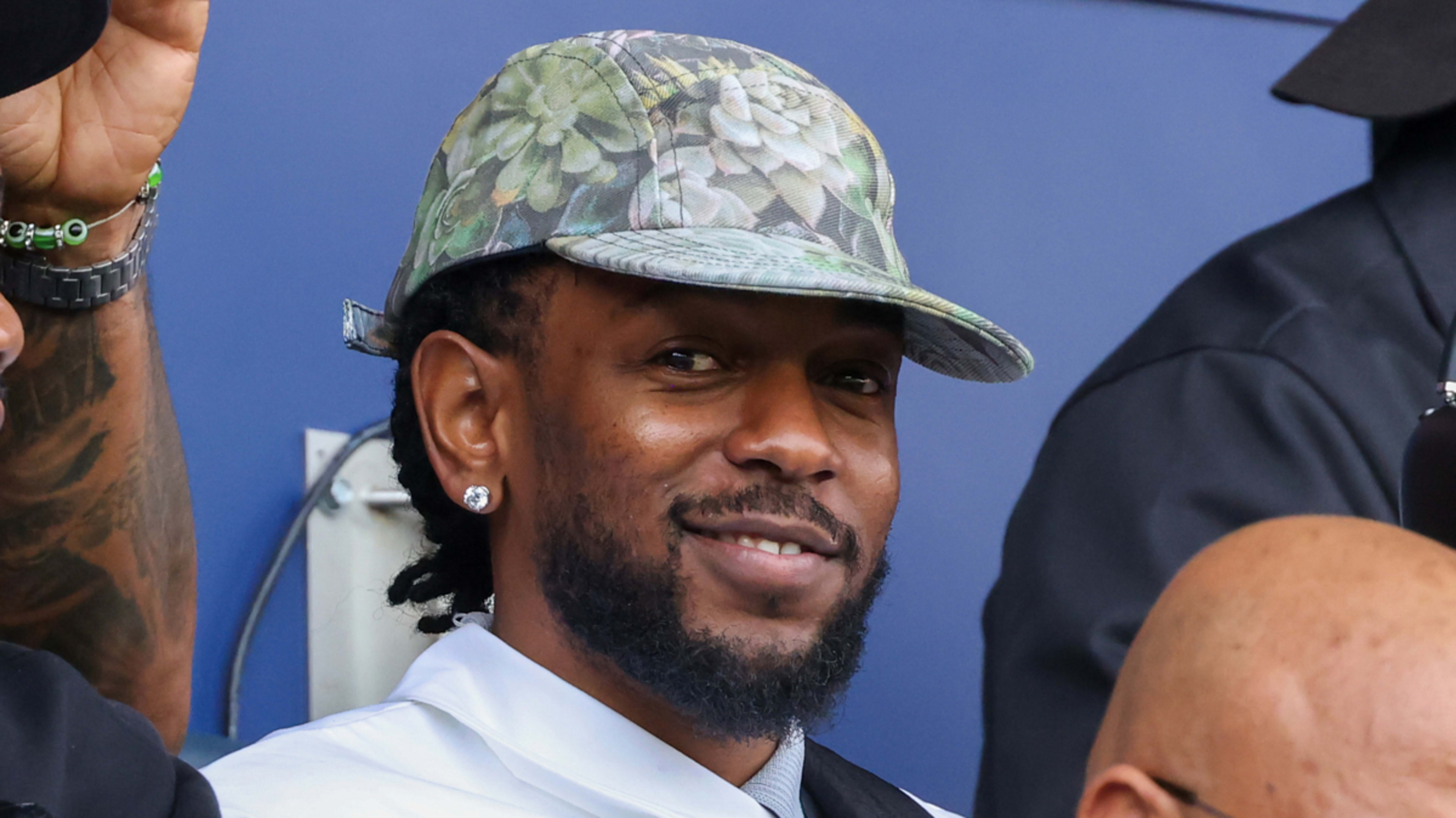 Kendrick Lamar smiles while wearing a patterned cap and earrings