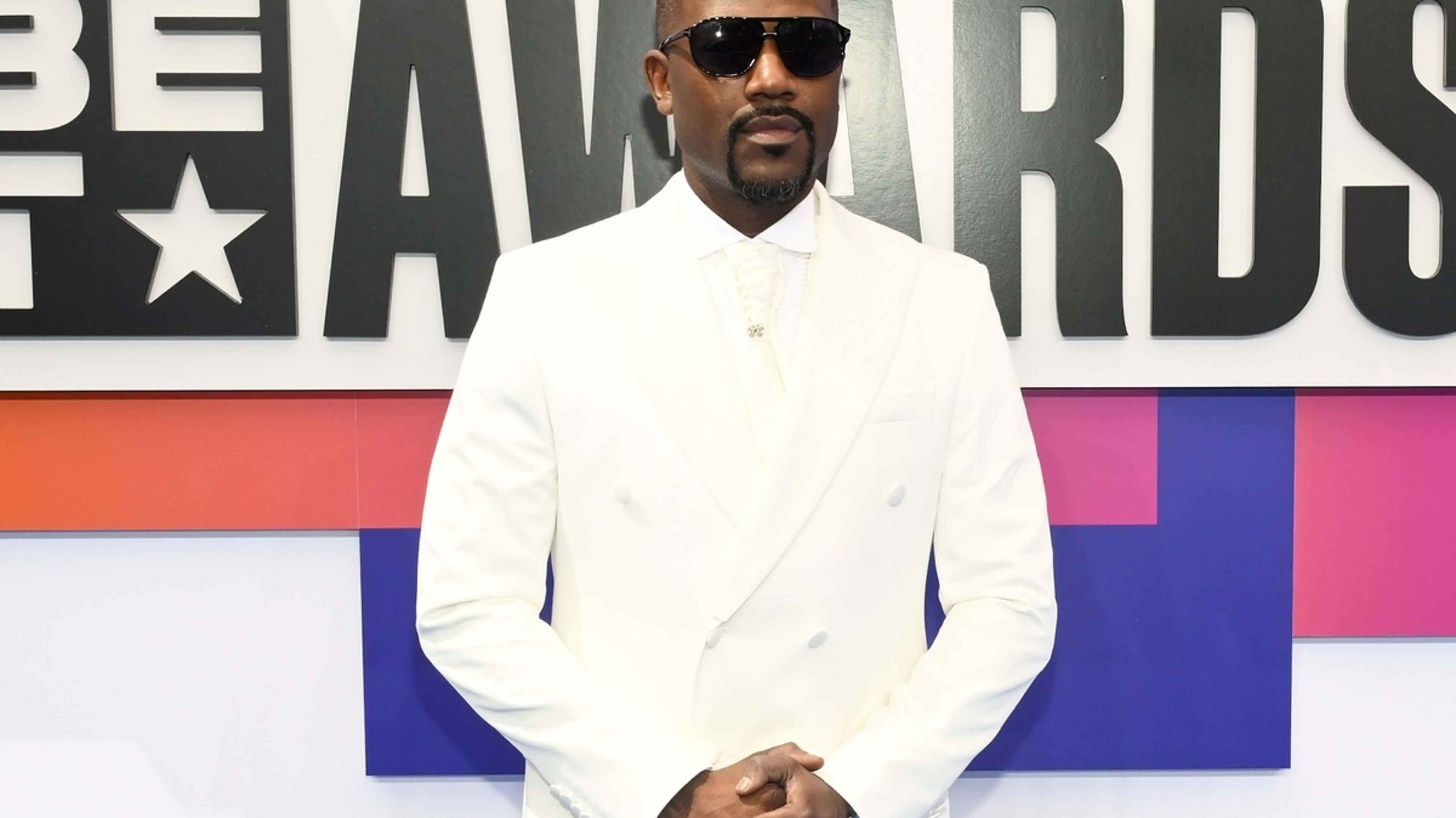 Ray J stands on the BET Awards red carpet in a classic white suit with a tie and sunglasses