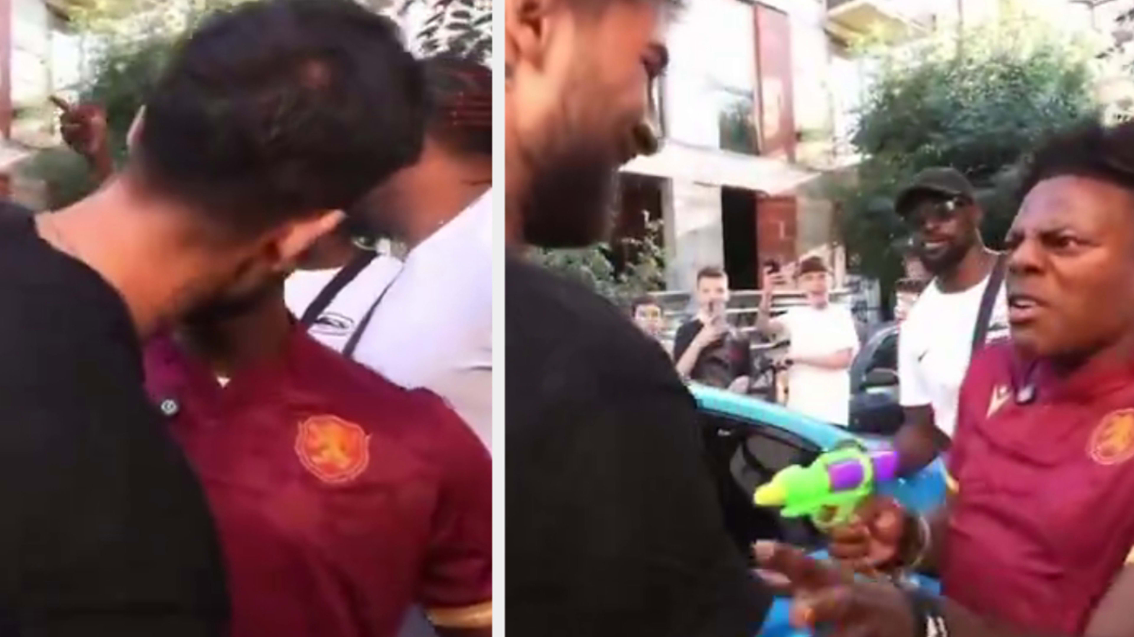 Group of individuals in a street, one holding a toy water gun. People around them are watching and smiling