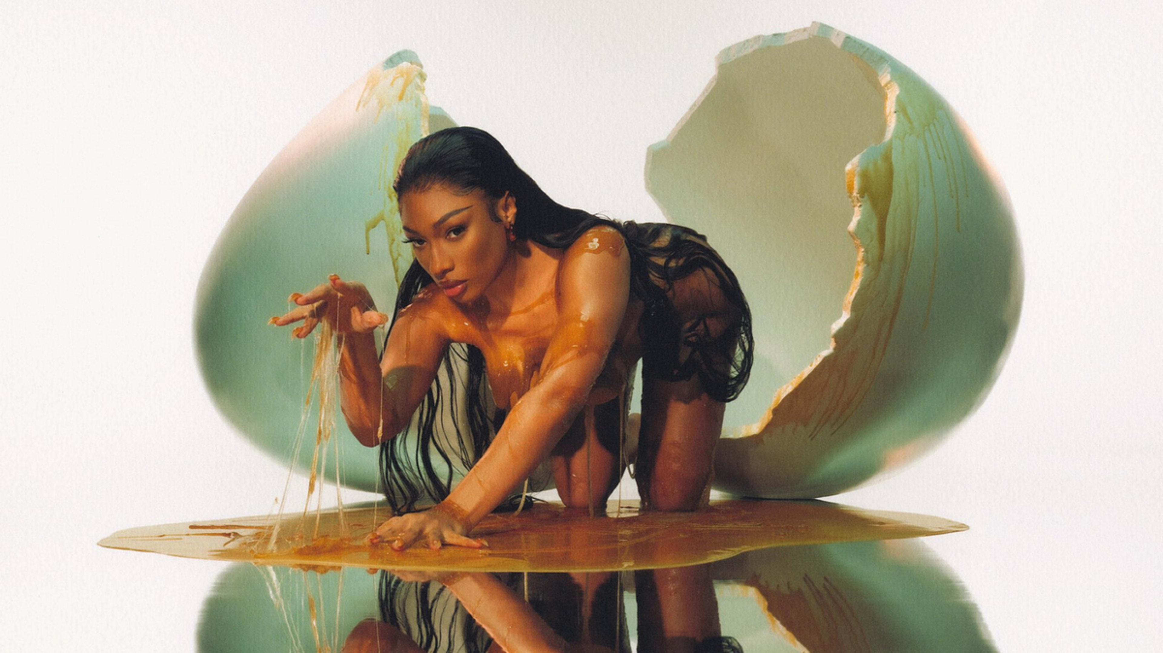 Megan Thee Stallion poses on all fours in front of a giant cracked egg, covered in a liquid resembling yolk