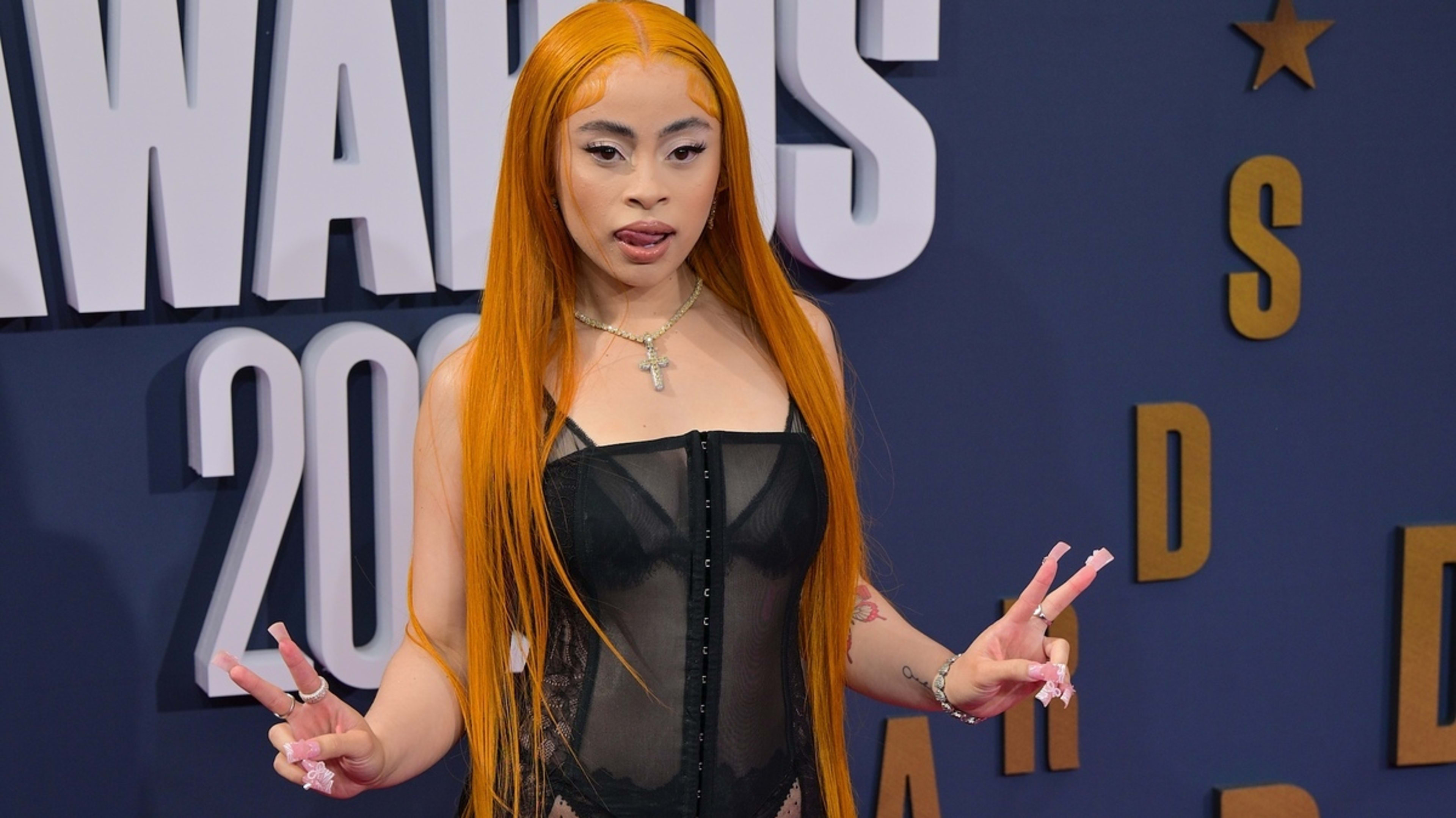 Ice Spice poses on the red carpet wearing a sheer black outfit and holding up peace signs at a music awards event