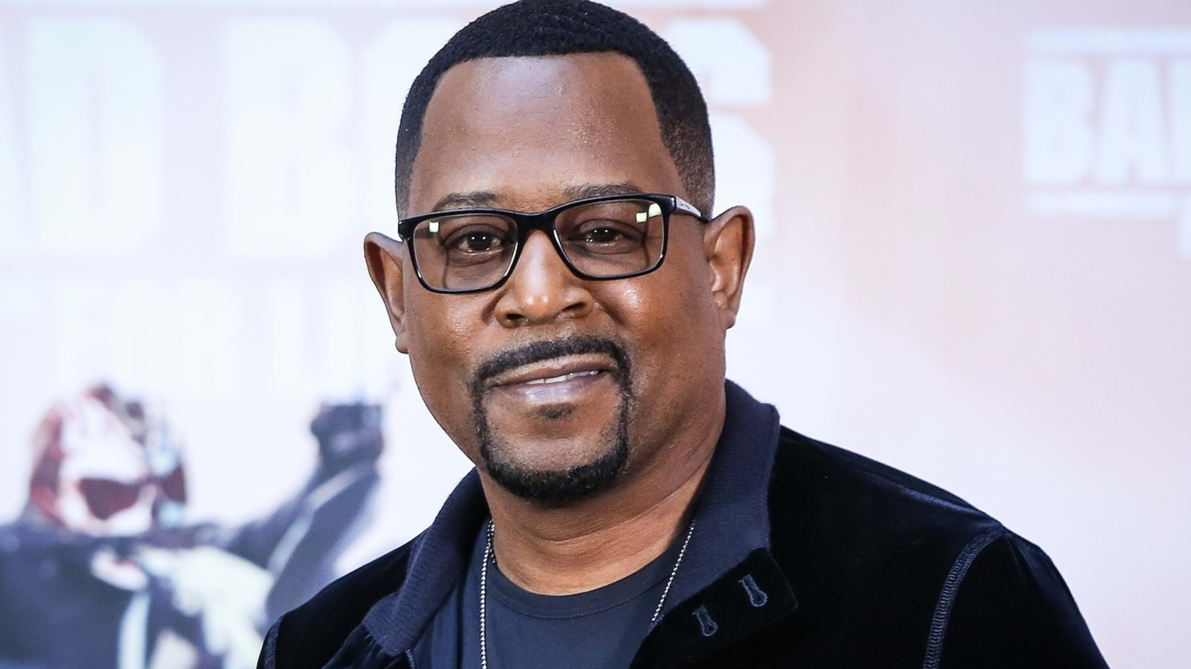 Martin Lawrence smiles on the red carpet, wearing a dark jacket over a t-shirt and glasses, at the premiere of Bad Boys for Life