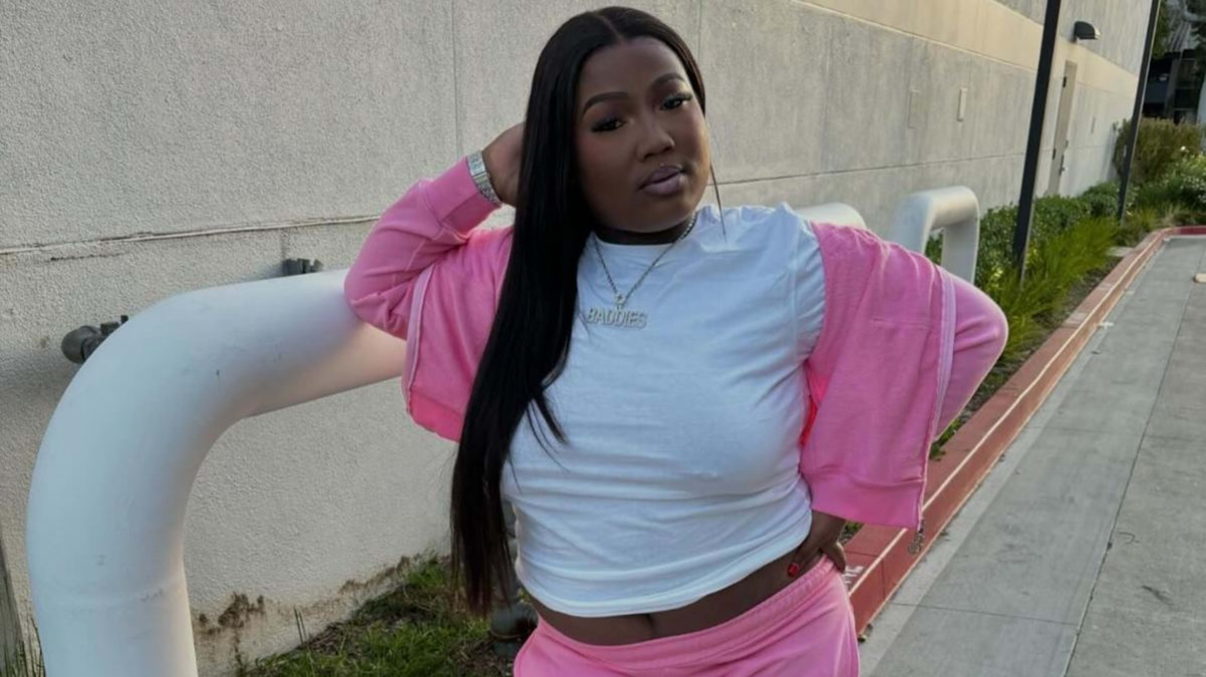 Woman posing outdoors, wearing a white crop top and pink jacket and pants