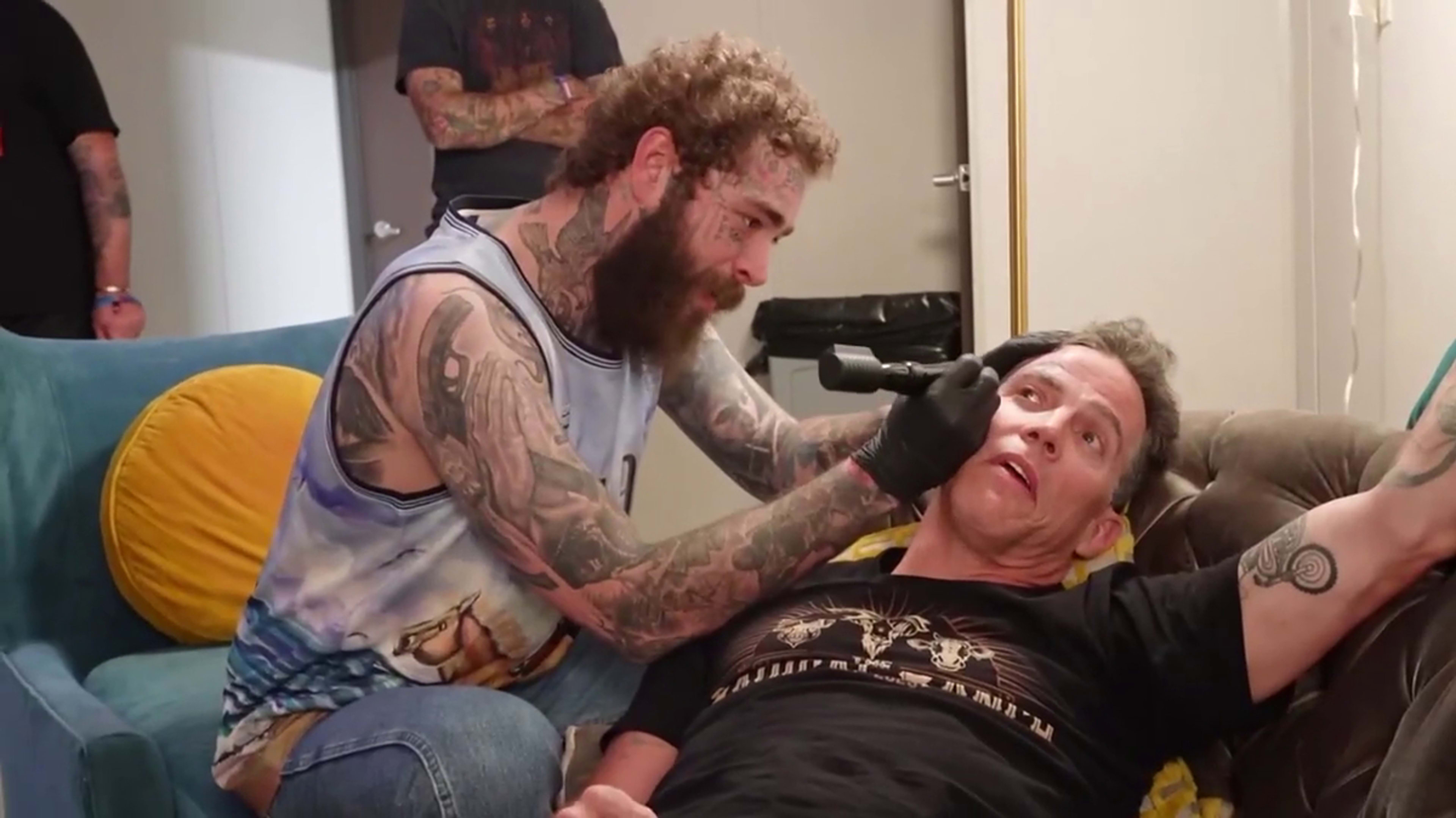 Post Malone giving Steve-O a tattoo on his face as they both sit in a room