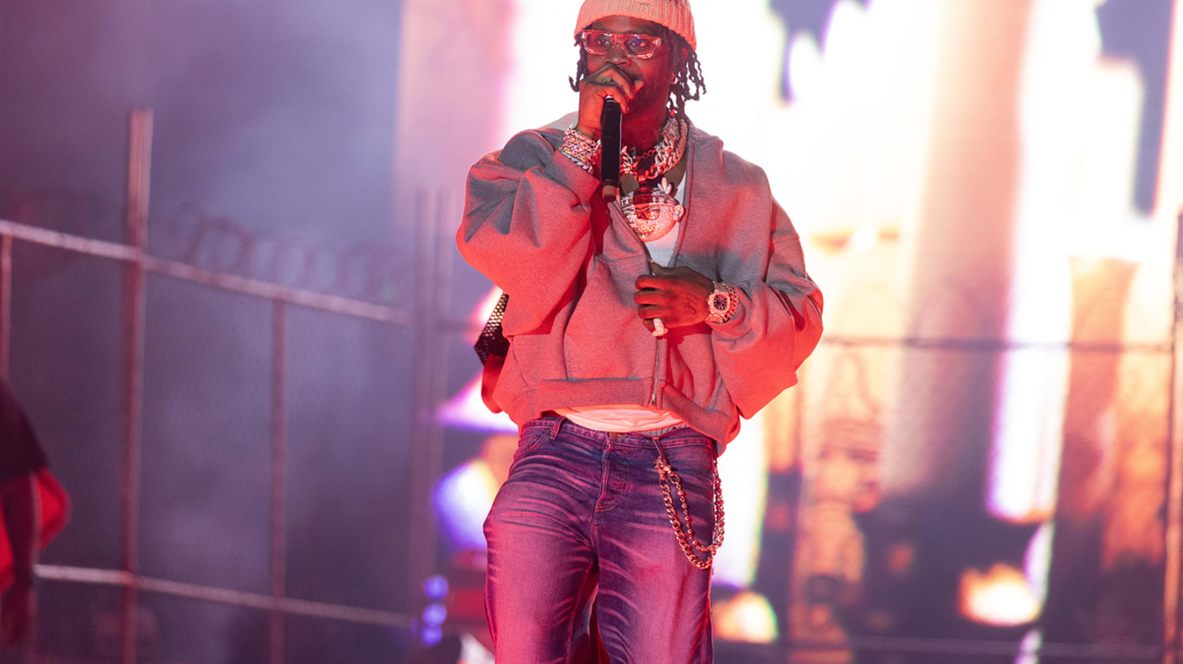 Offset performing on stage wearing a baggy sweatshirt, large chain necklaces, and sunglasses