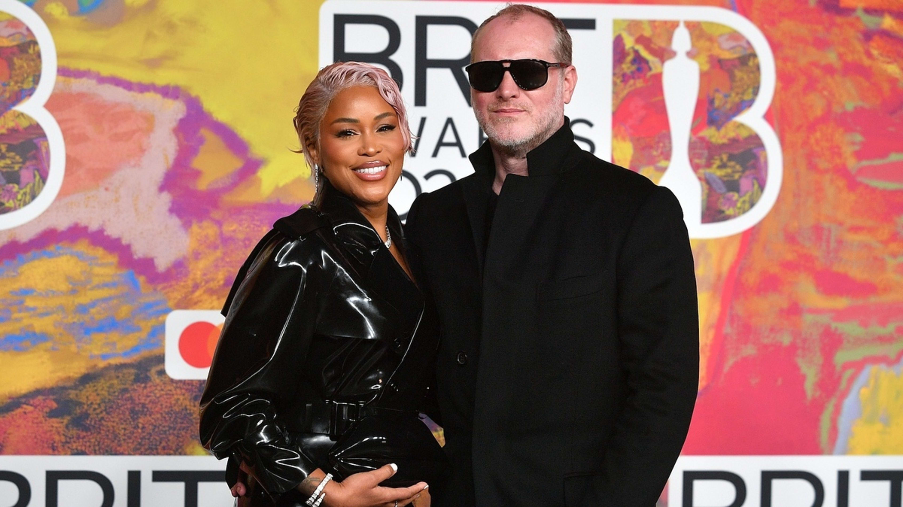 Eve and Maximillion Cooper pose at the BRIT Awards. Eve wears a shiny black jacket, and Maximillion is in a black coat and sunglasses