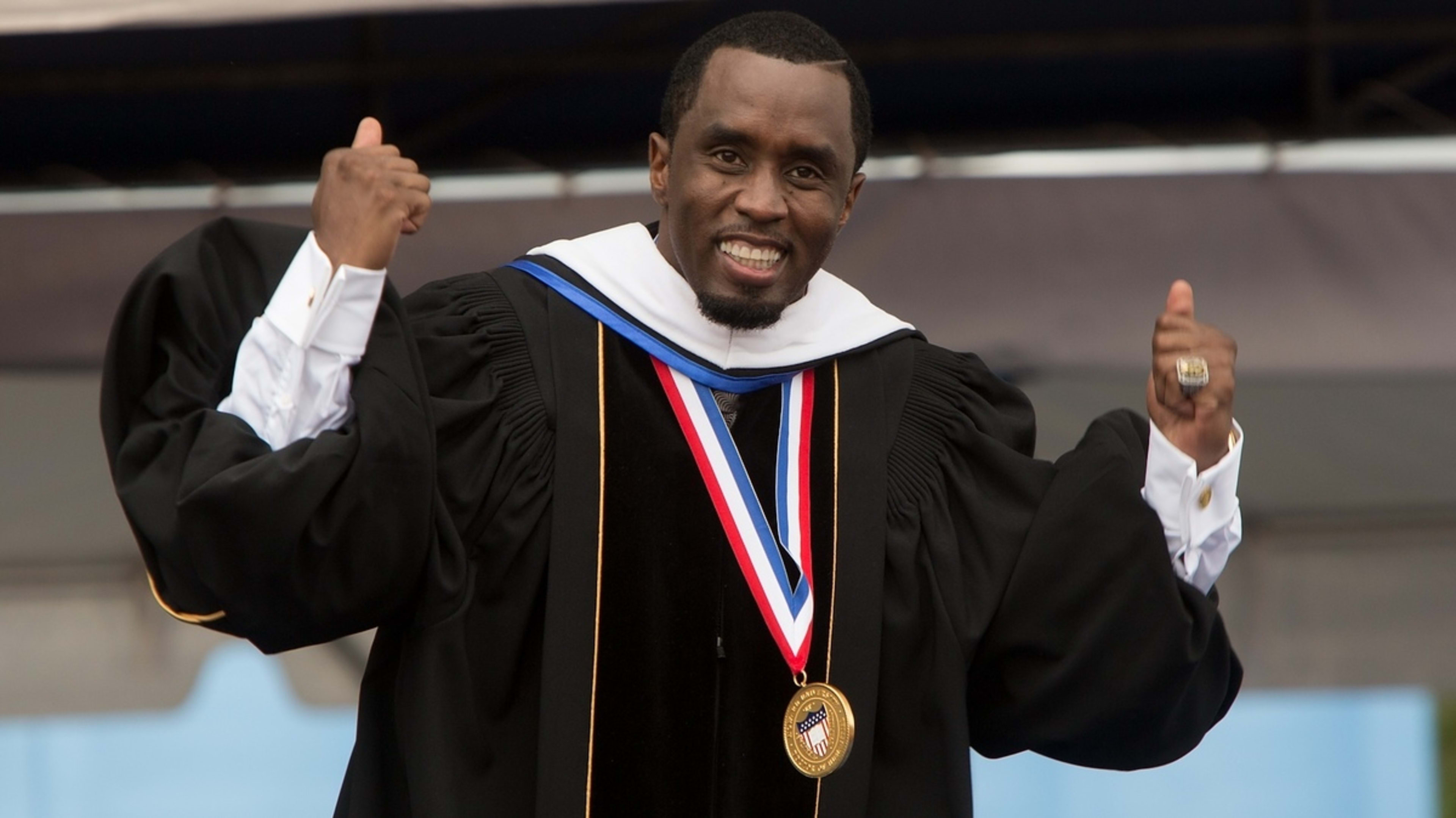 Sean "Diddy" Combs is wearing academic regalia and a medal, smiling and raising both fists in the air