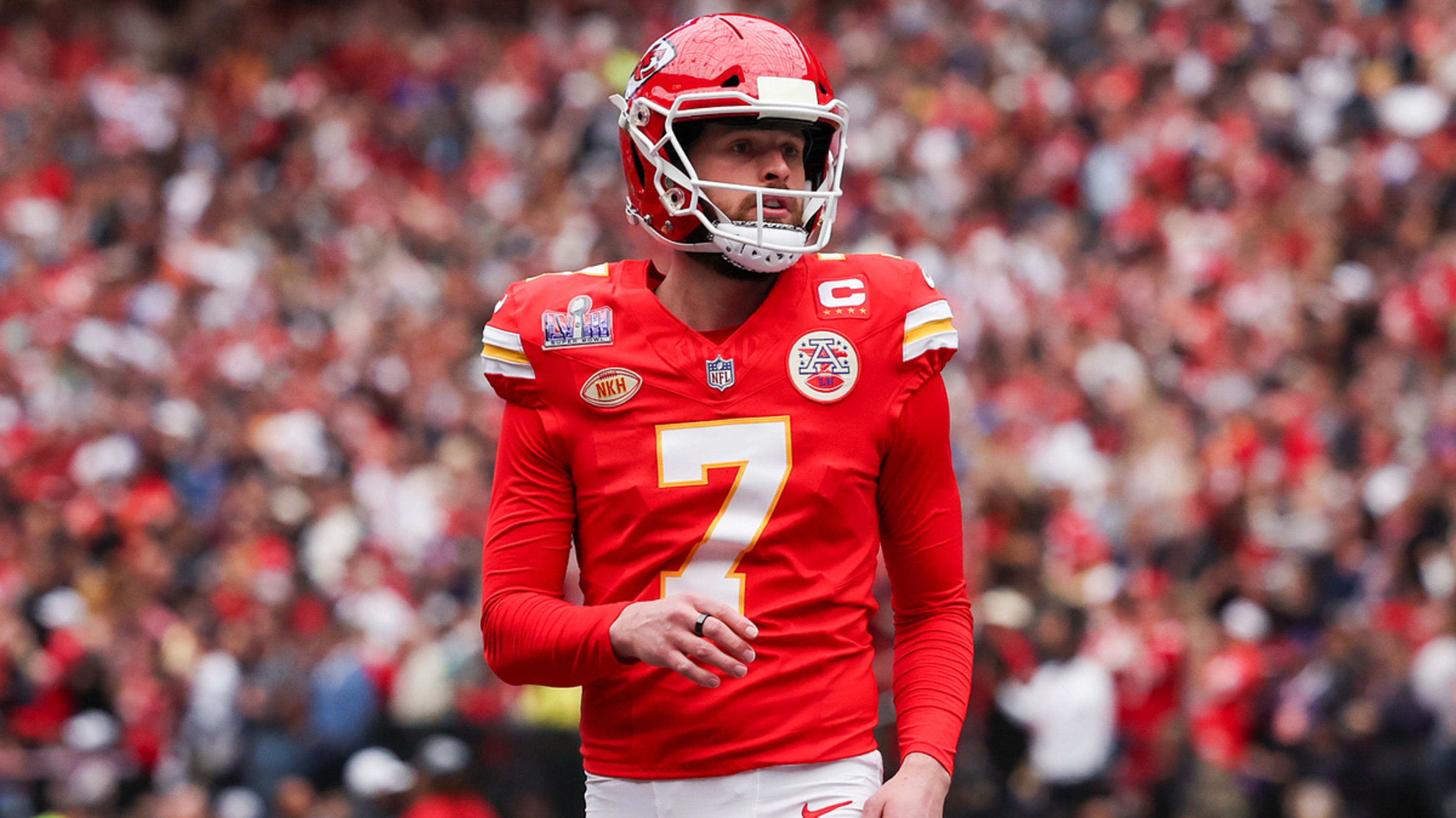 Athlete in football uniform with captain's 'C' patch on field, helmet in hand