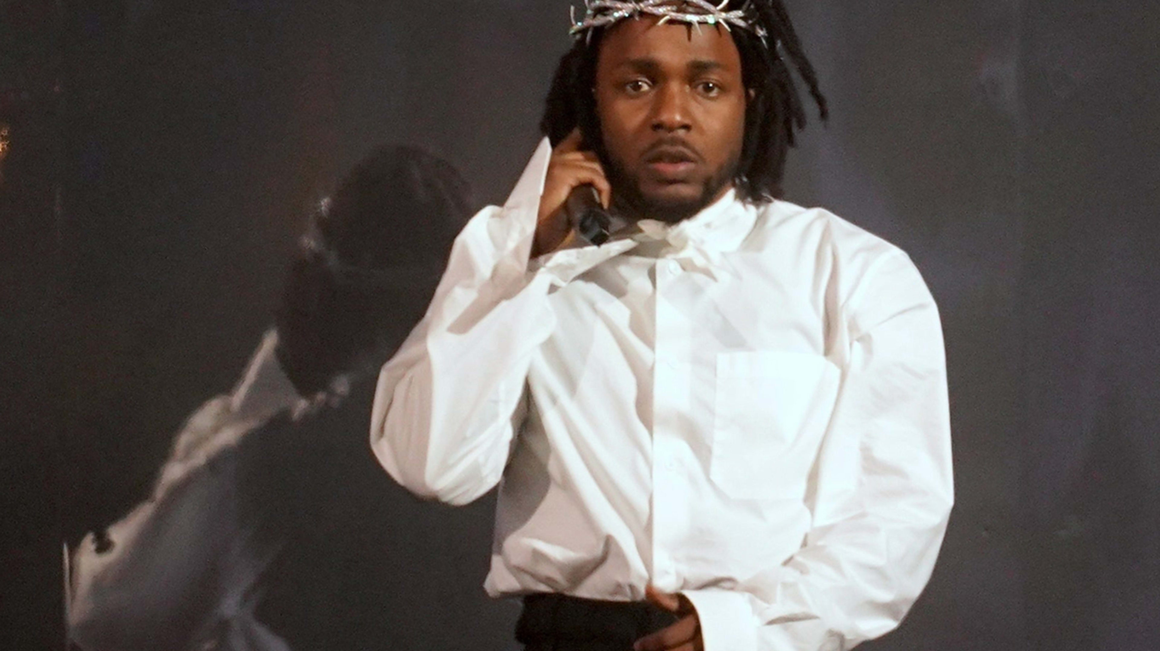 Music artist in a white shirt performs onstage with a microphone, adorned with a symbolic crown